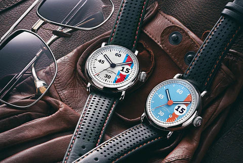 Two watches with colorful faces on a brown leather surface with sunglasses.