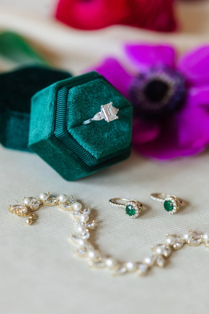collection of jewelry pieces with diamonds, pearls, and emeralds with green box and blurred background