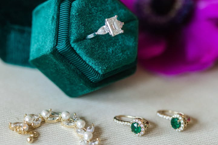 Jewelry set including rings and a necklace on a white surface with flowers in the background.