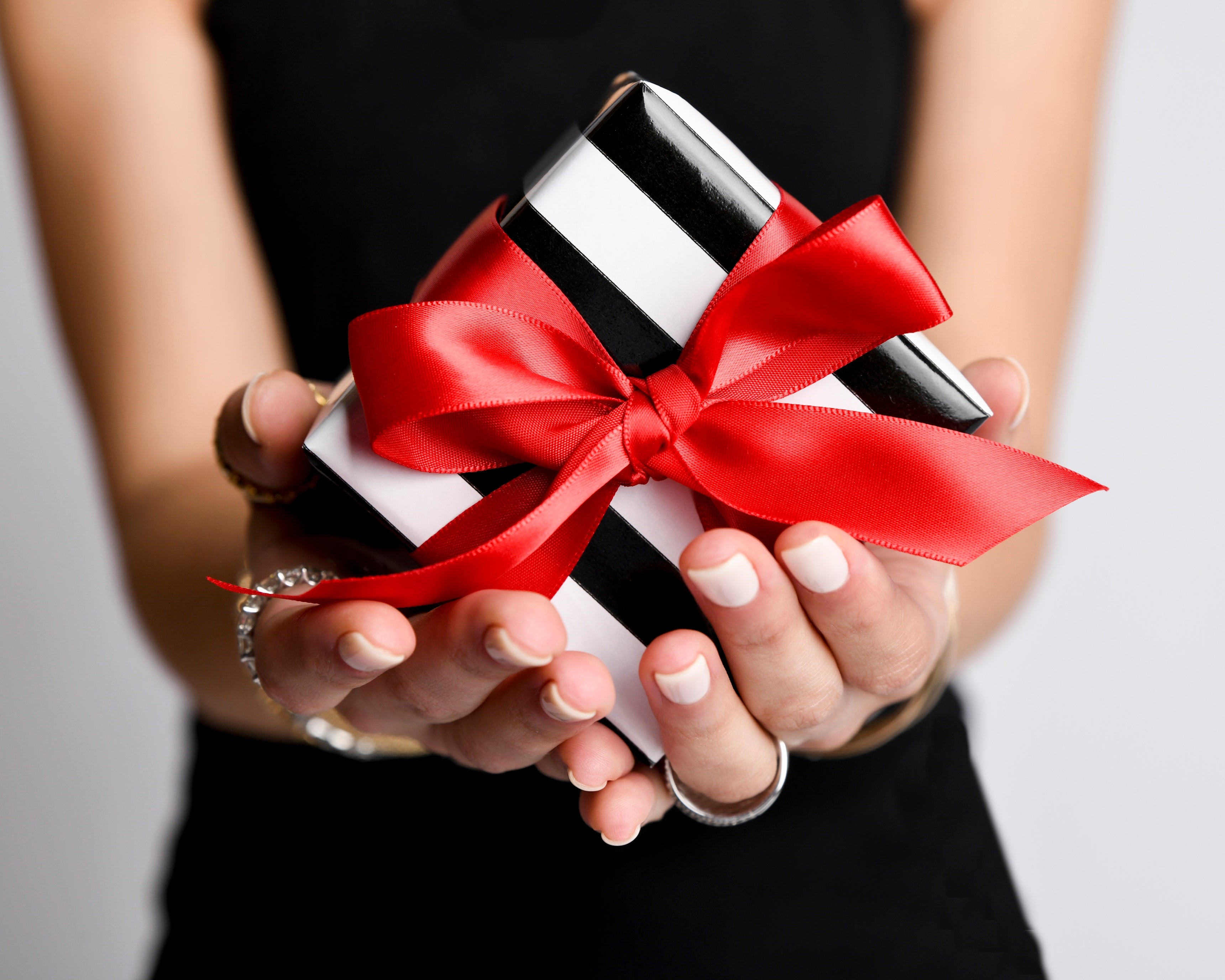 Person holding a black and white gift box with a red ribbon against a neutral background