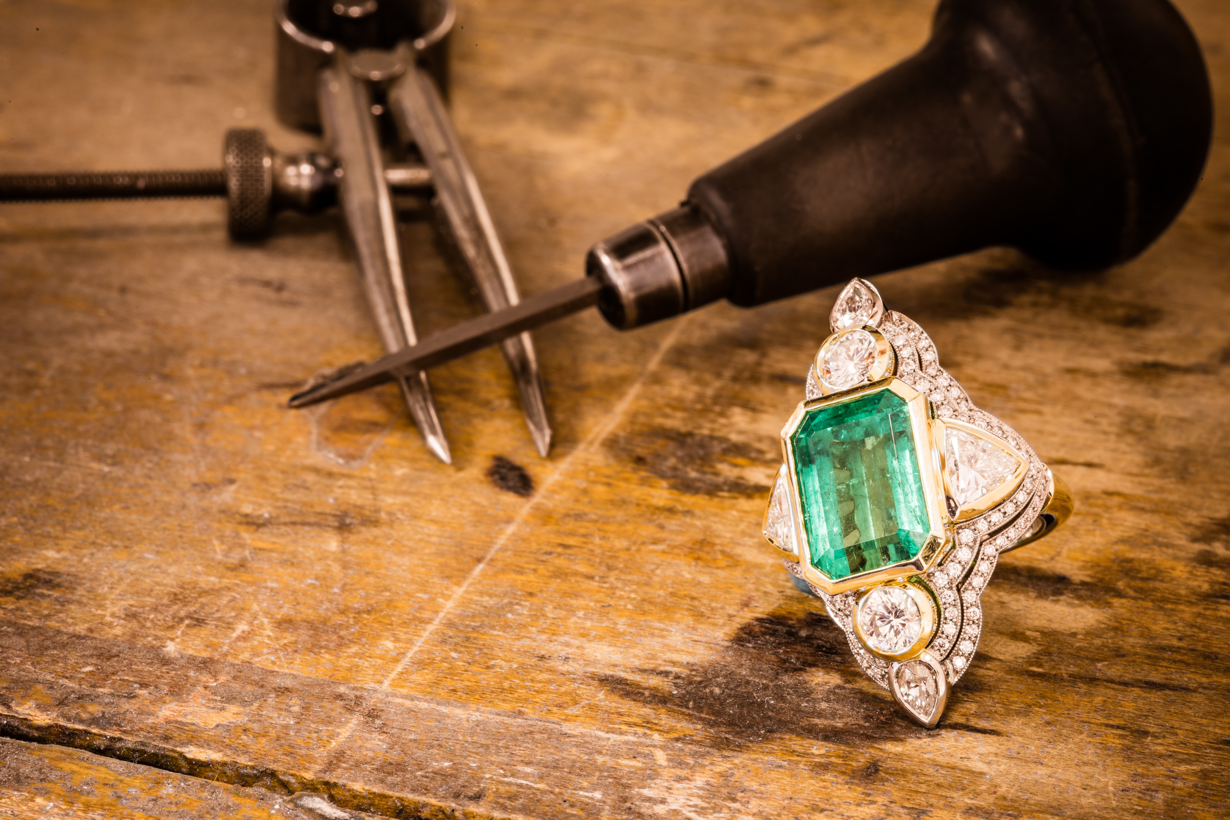 Emerald ring on a wooden surface with jewelry tools in the background