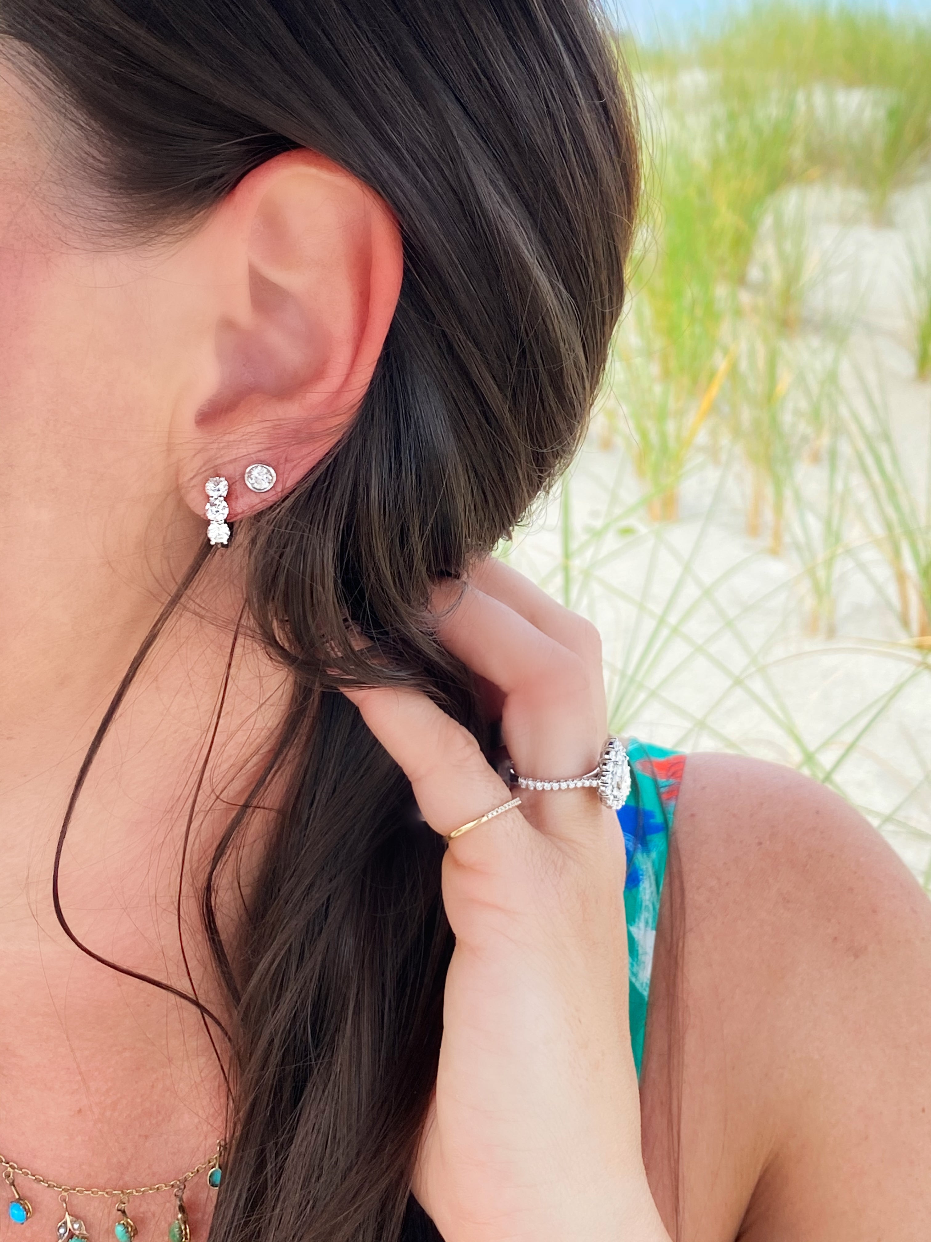 Close-up of a woman's ear with earrings, hand touching hair, beach background