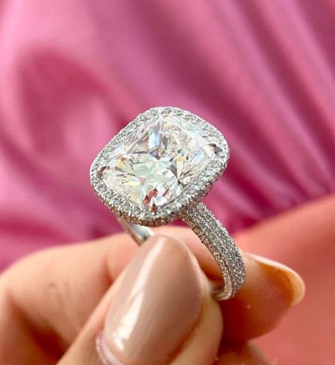 hand holding large diamond ring in front of pink blurred background