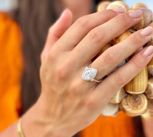 hand with marquise diamond ring in front of blurred orange background
