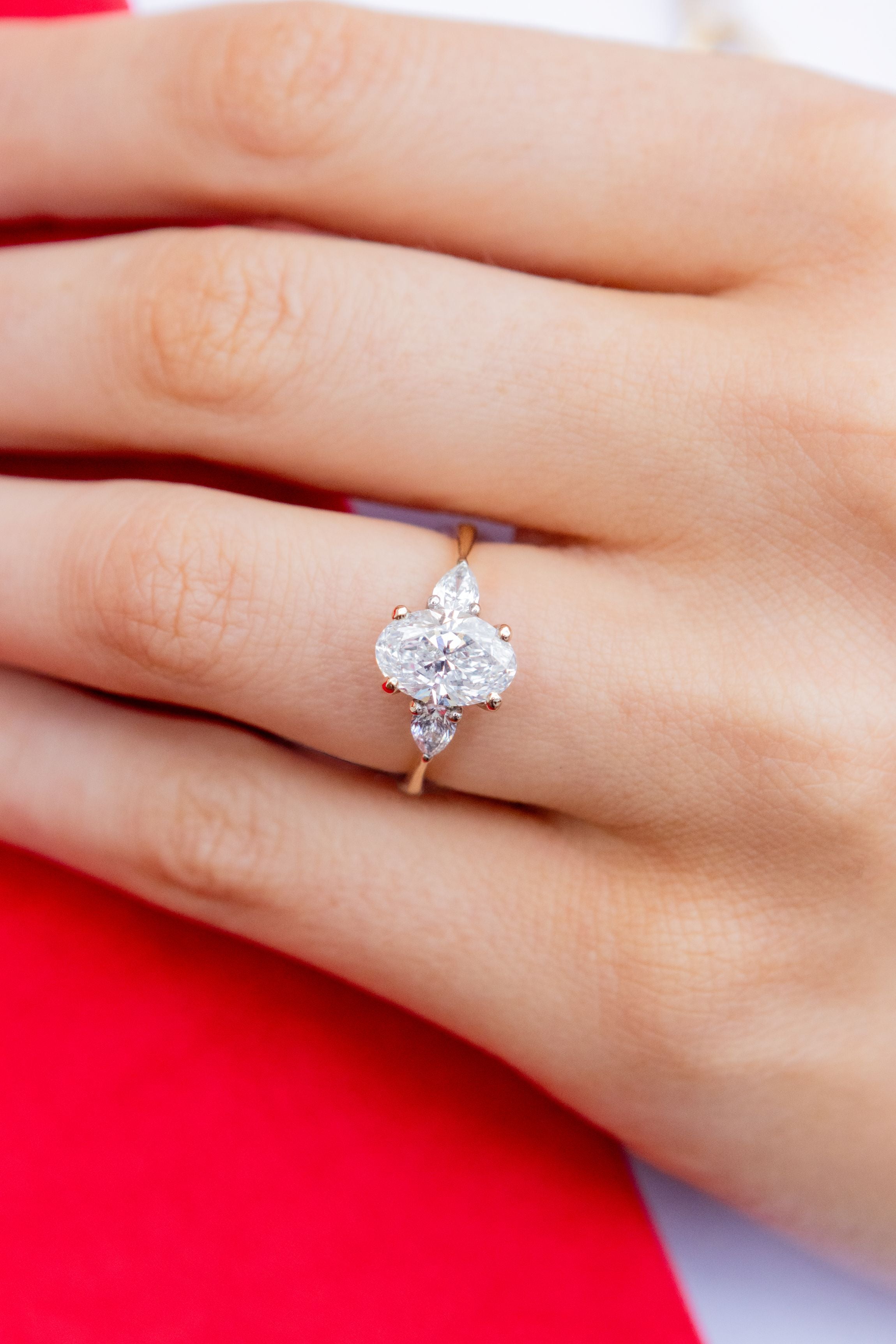 oval-shaped diamond ring on a hand with a red background
