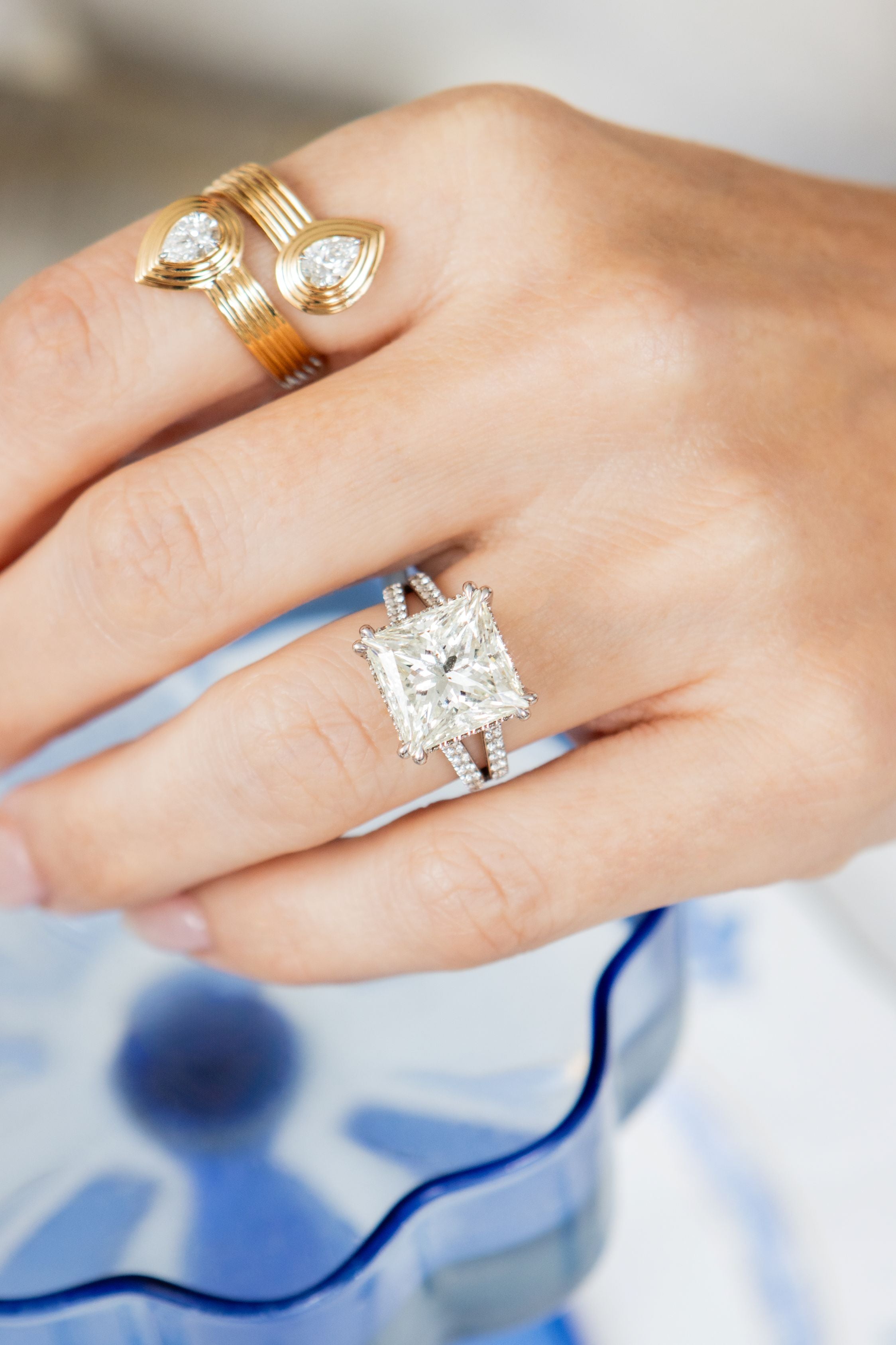 hand wearing diamond and gold rings with blurred blue and white background
