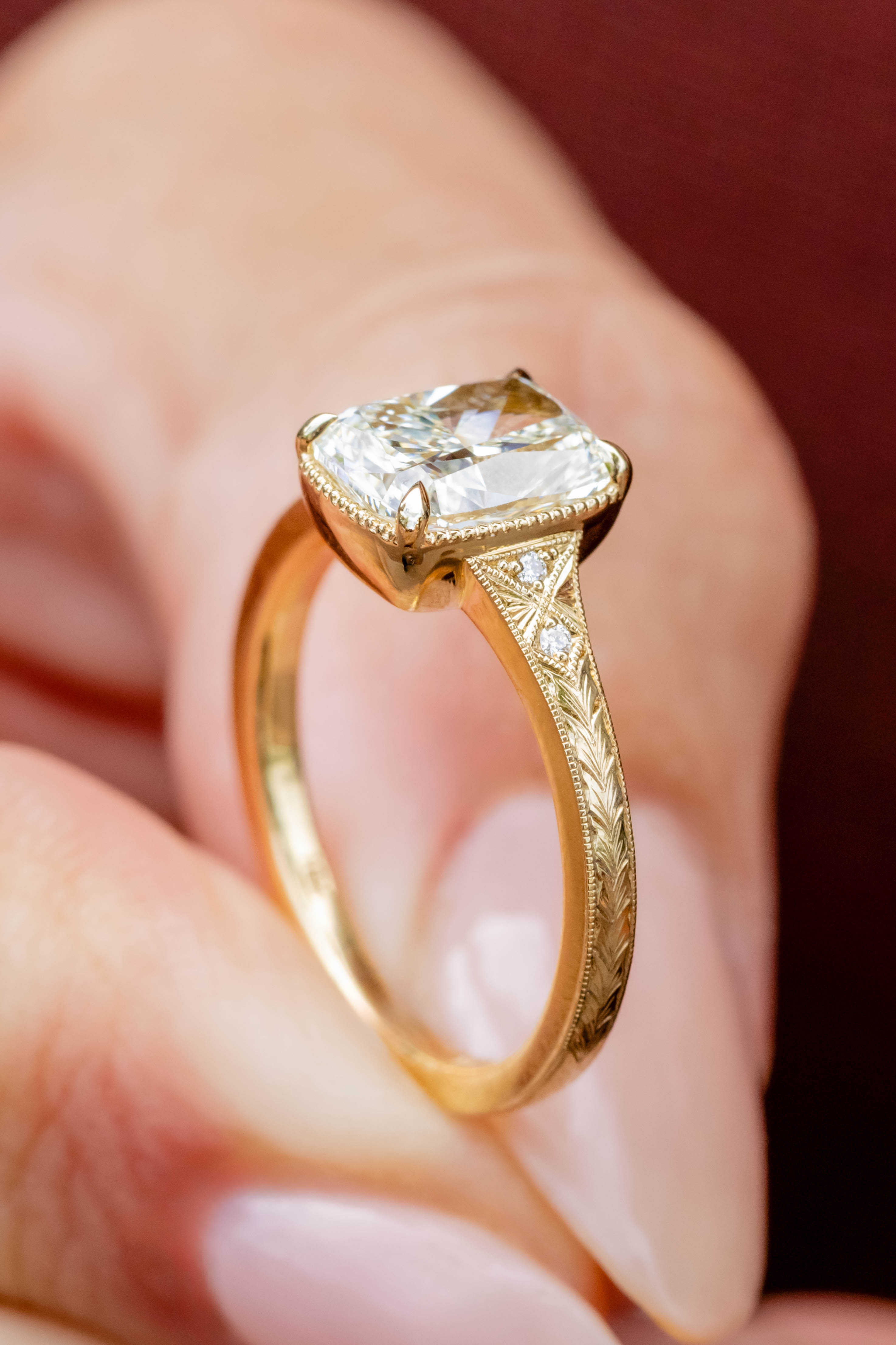 Gold ring with a large diamond held between fingers against a blurred background