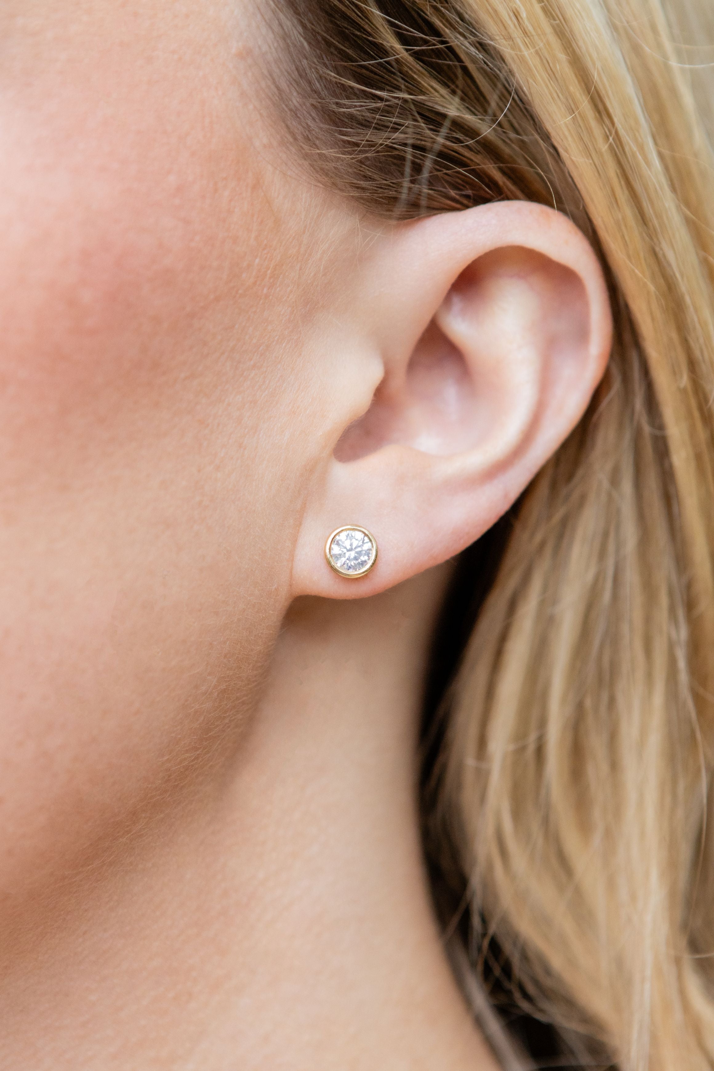 Close-up of an ear wearing a diamond stud earring with blonde hair.