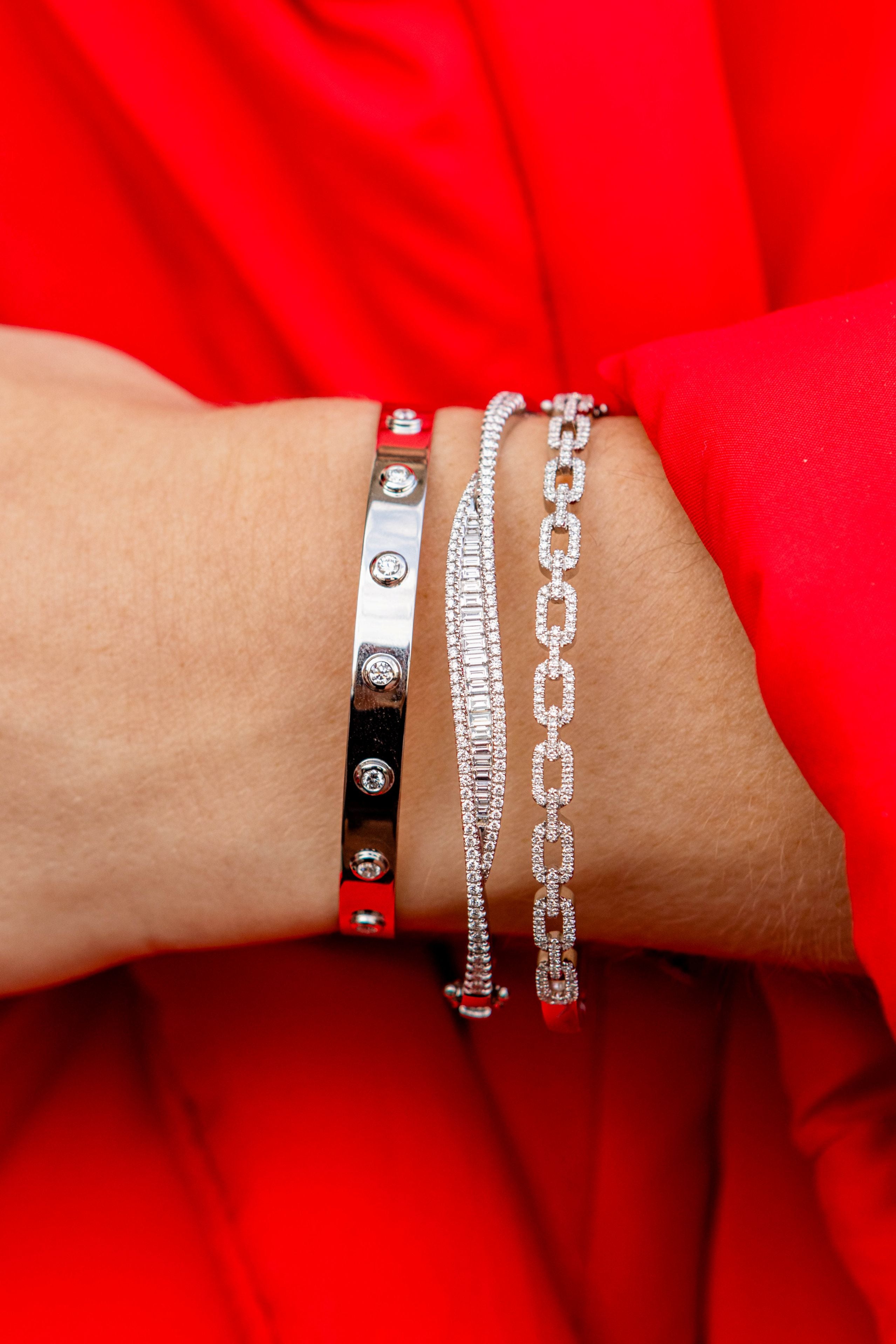 Close-up of a wrist wearing three silver bracelets against a red background