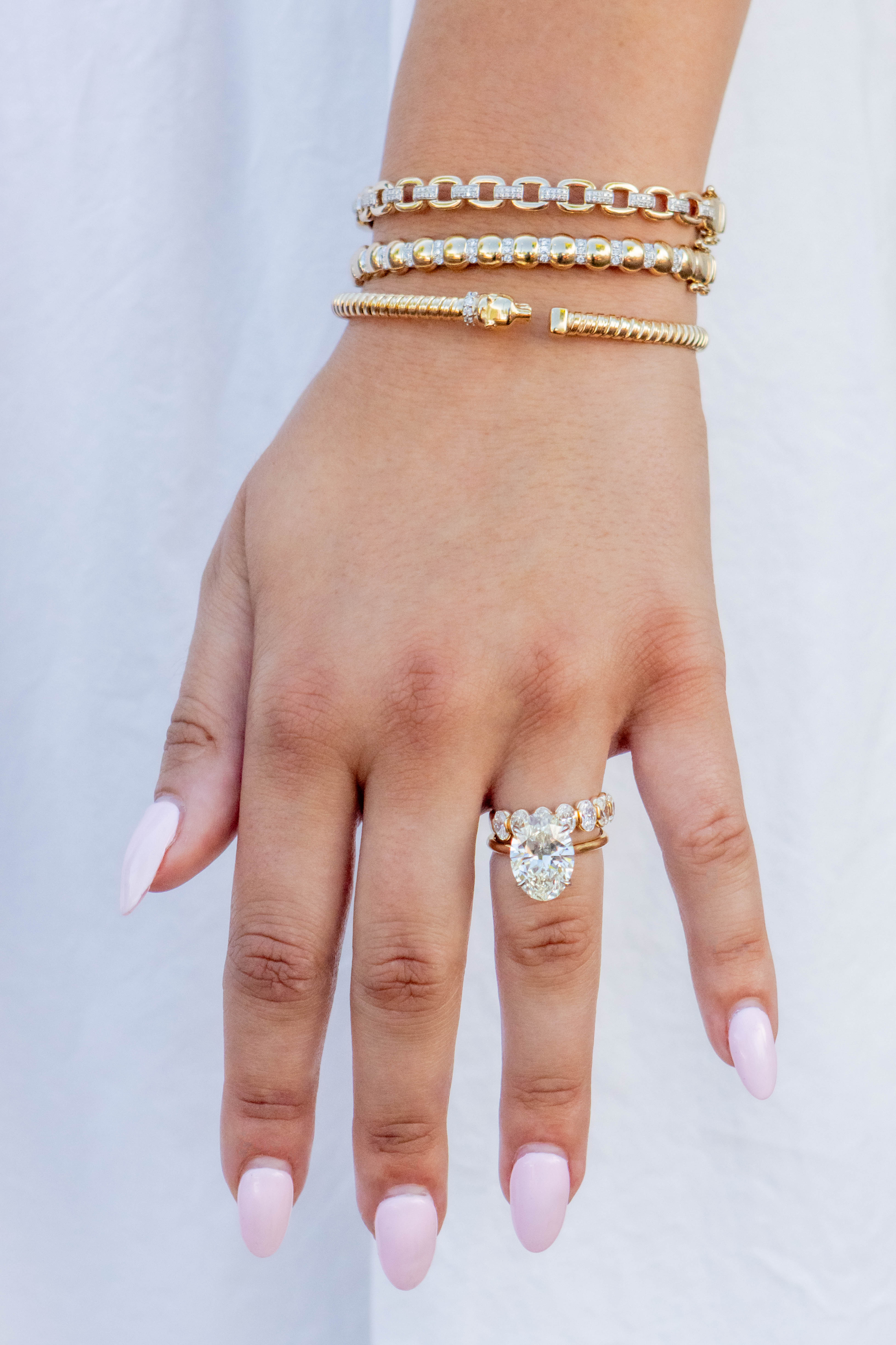 Hand wearing a diamond ring with gold bracelets on a light background