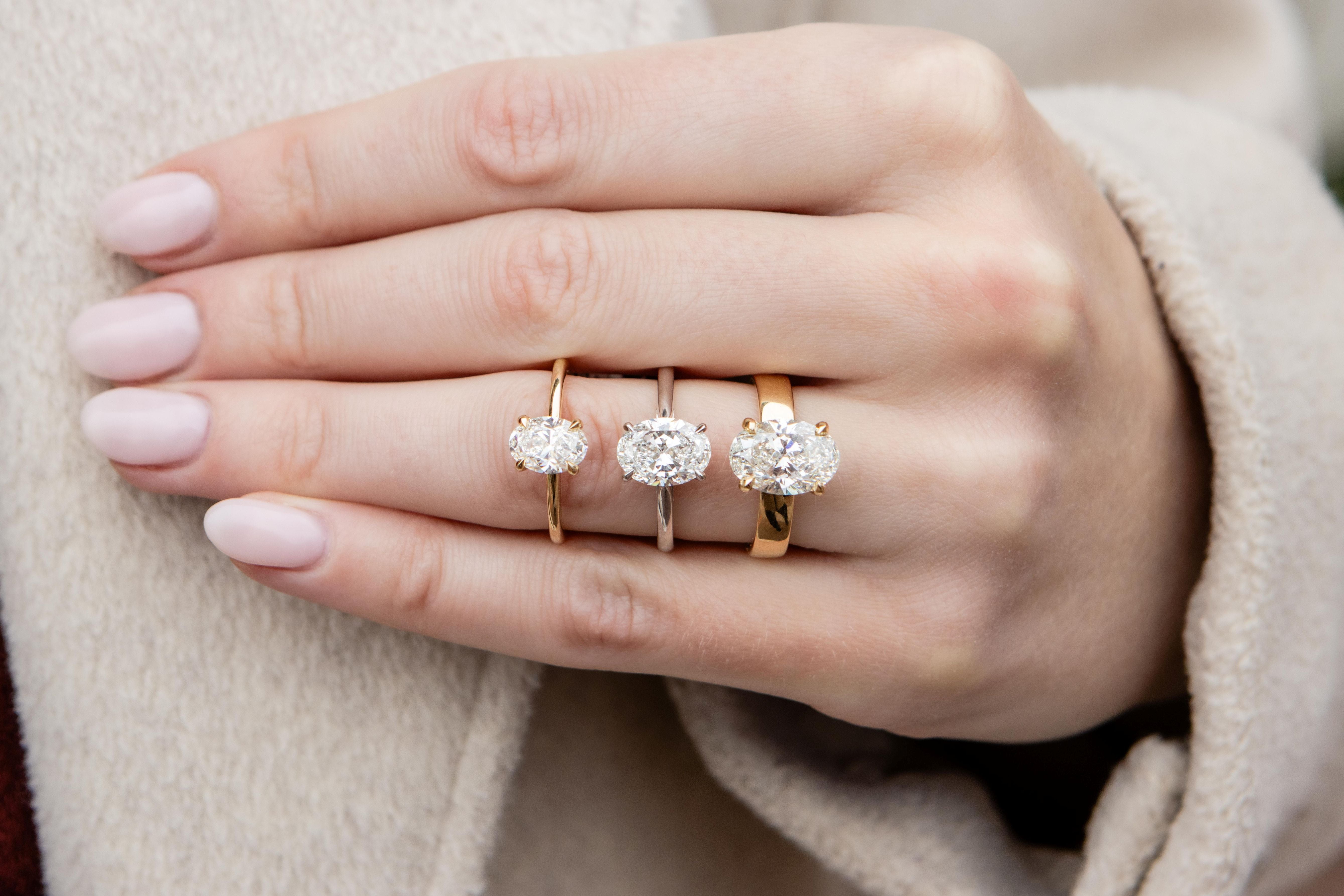 Hand wearing three diamond rings on a neutral background