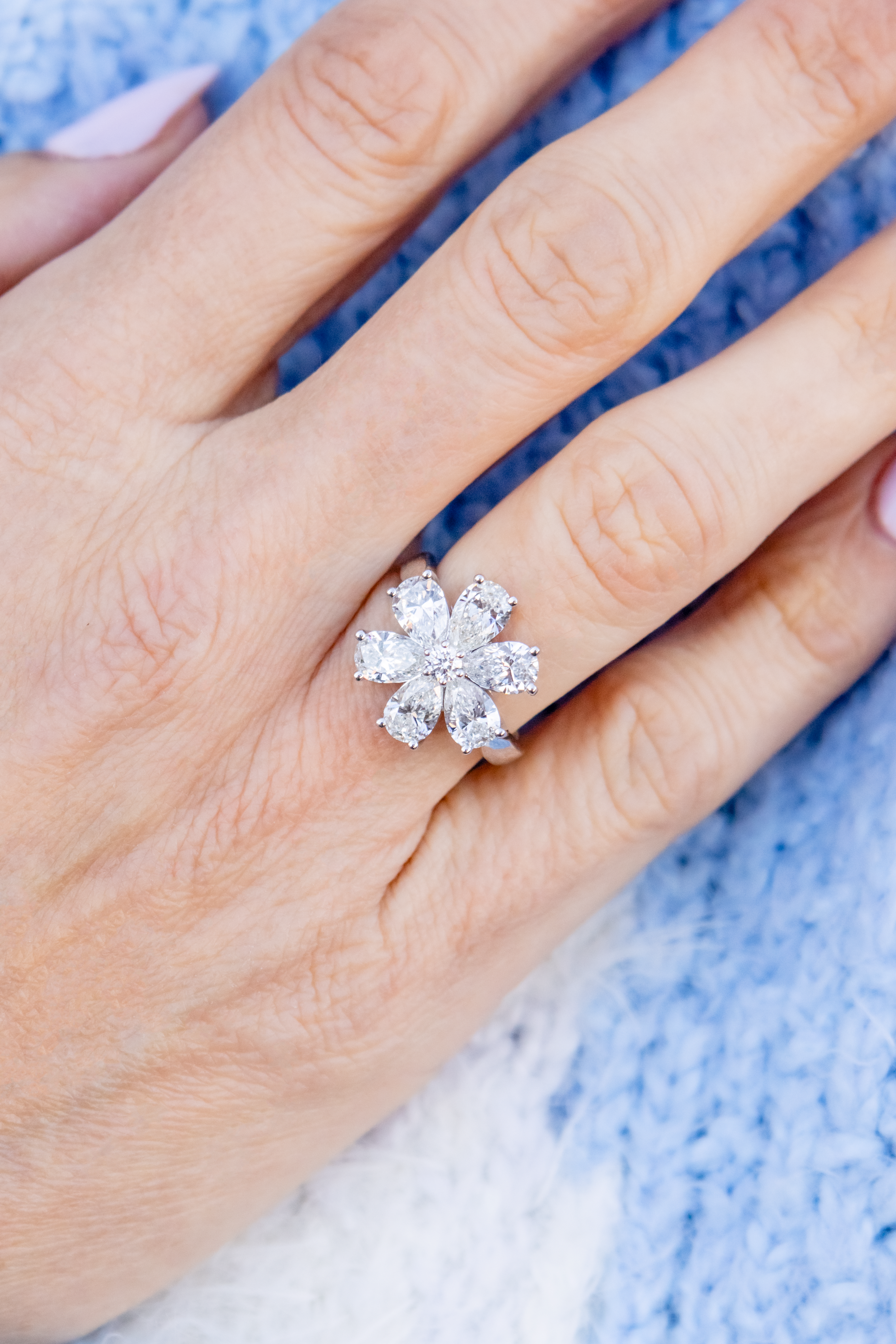Close-up of a hand wearing a flower-shaped diamond ring with a blue textured background