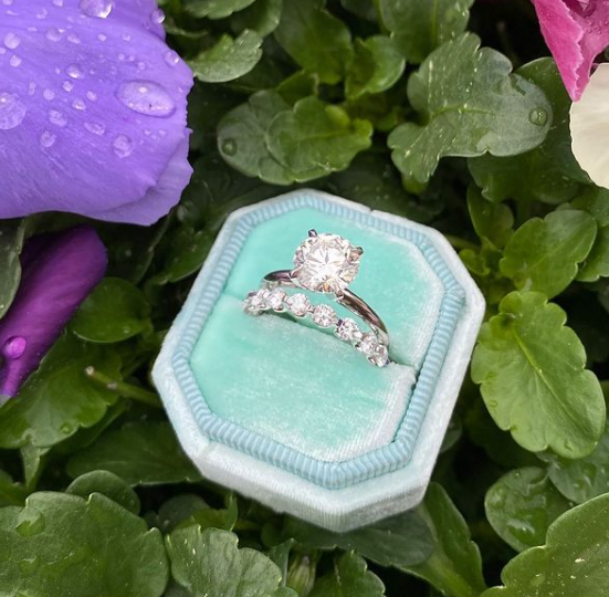 Diamond ring in a turquoise box on green leaves with purple flowers