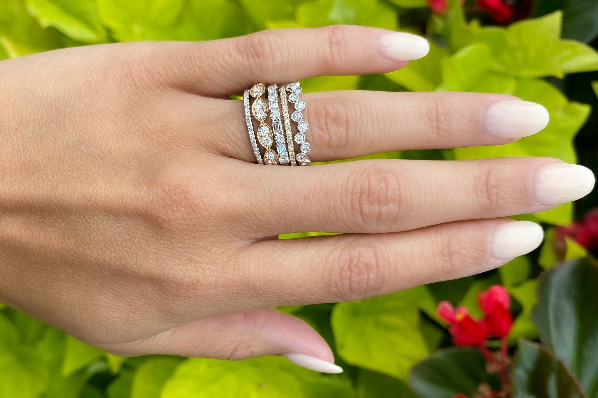 Hand wearing multiple diamond rings with a floral background