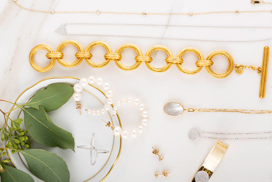Gold jewelry including a bracelet, ring, and earrings on a light background with green leaves.