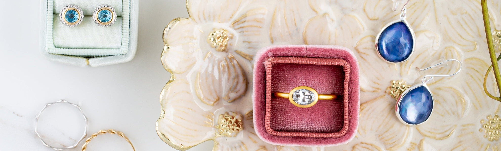 Gold ring with diamond in a pink velvet box on a decorative surface with earrings and jewelry.