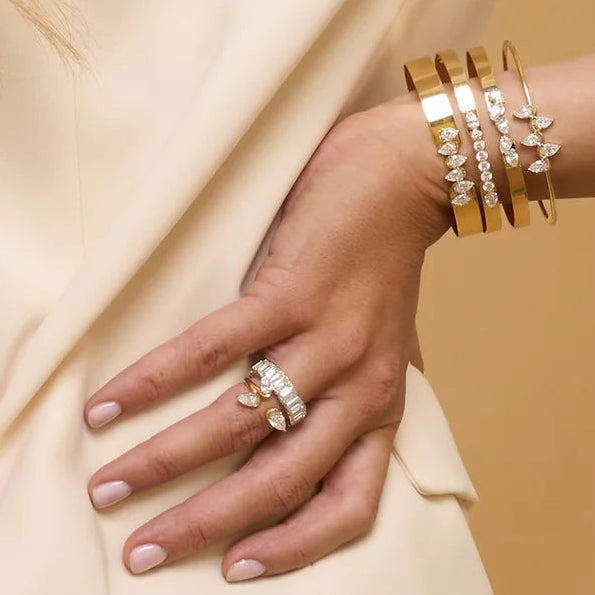 Close-up of hands with gold bracelets and rings on a beige background