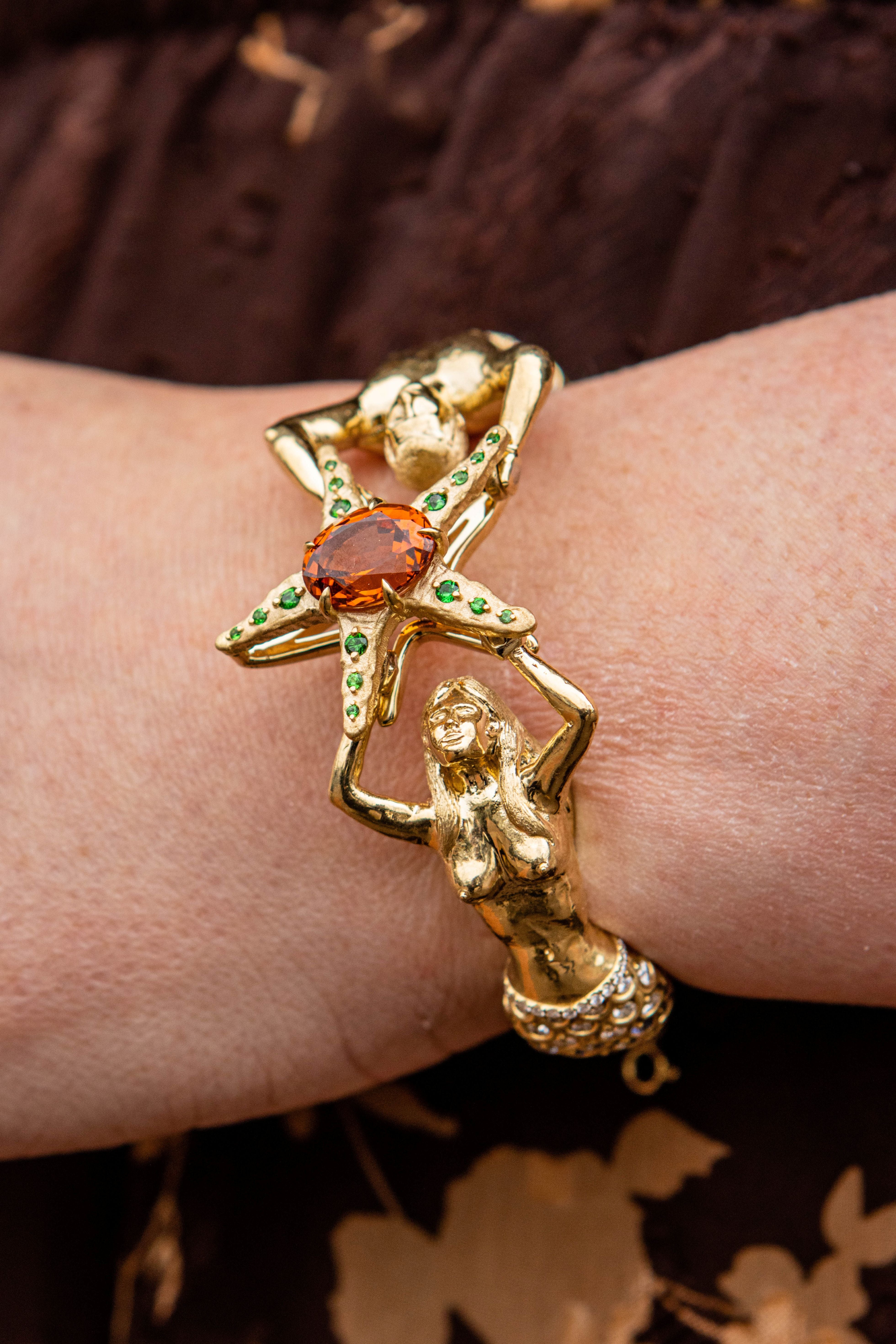 Starfish and mermaids gold custom bracelet with gemstones on a wrist with brown background