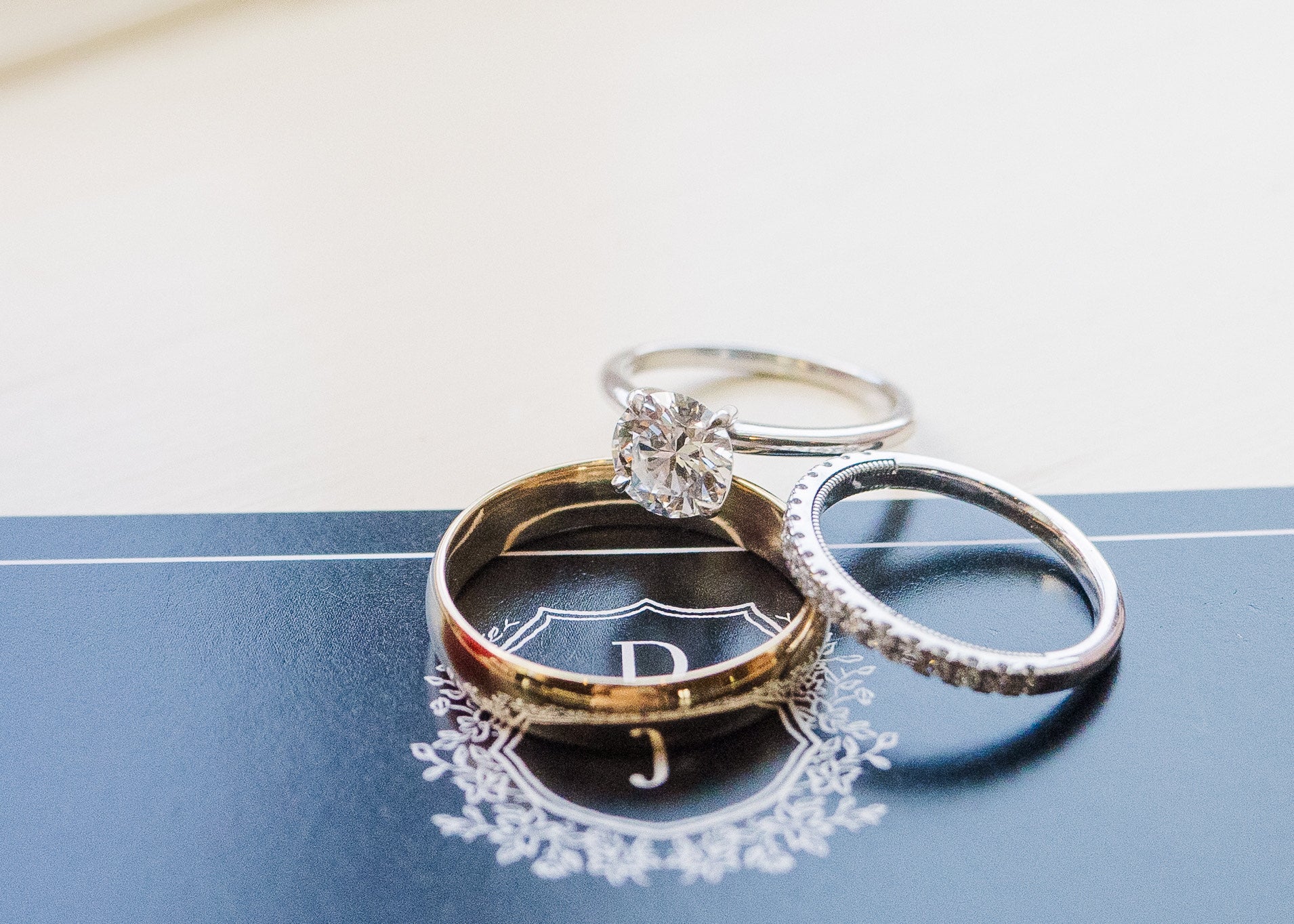 Two wedding bands, one gold and one silver, and one engagement diamond ring on a blue surface with a white background