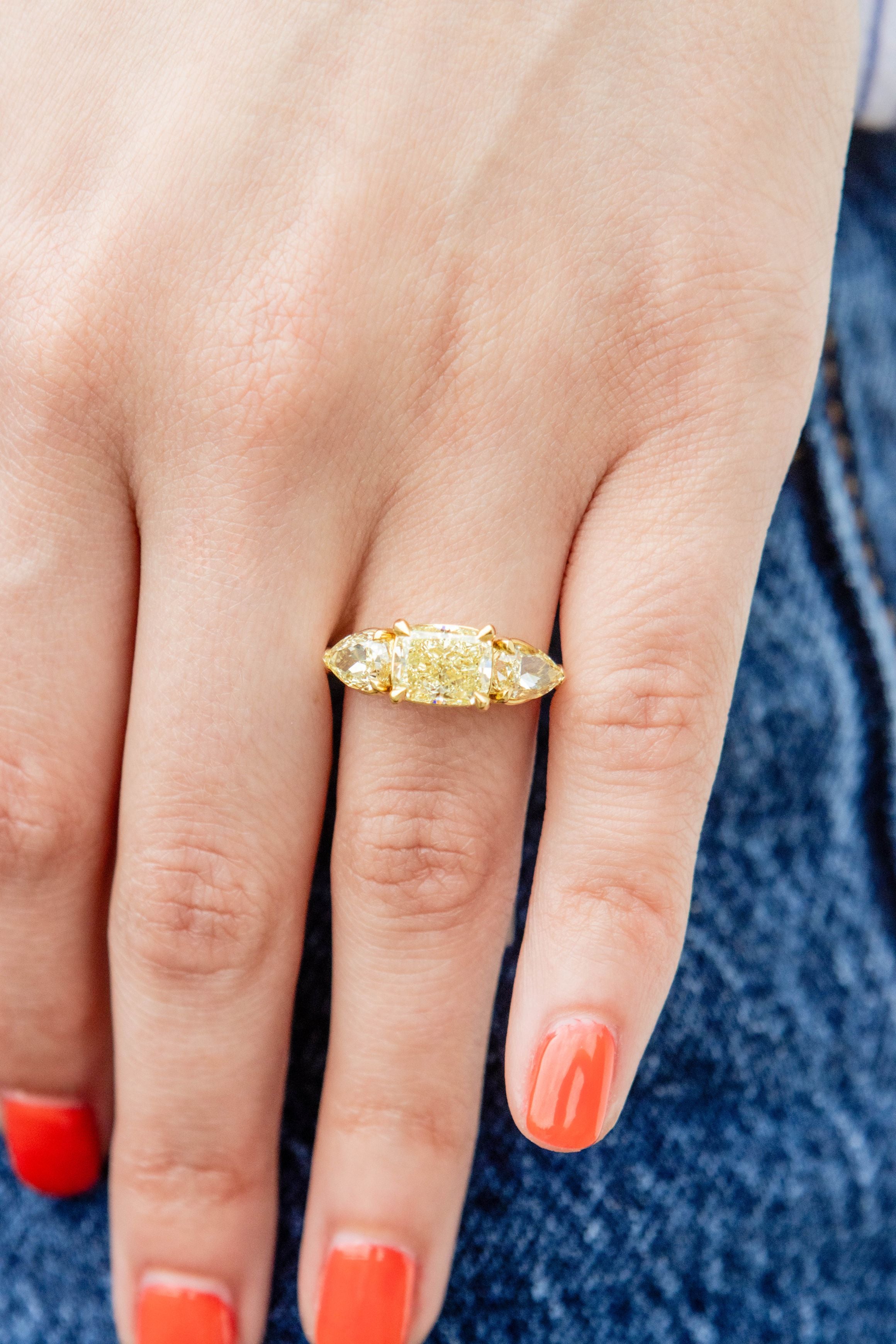 yellow diamond ring on a hand with red nail polish on a denim background