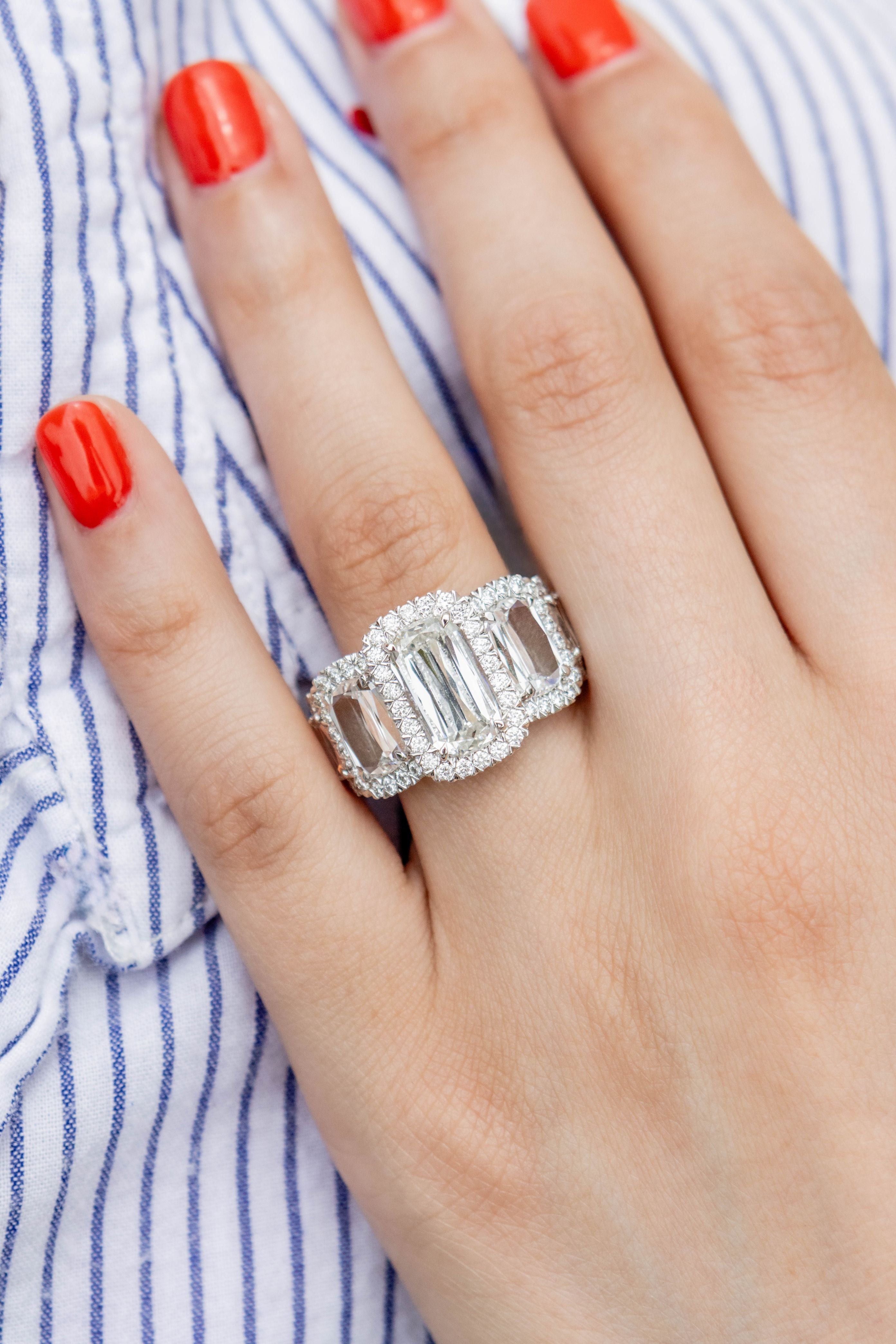 Silver ring with emerald-cut center stone on a hand with red nail polish against a striped background