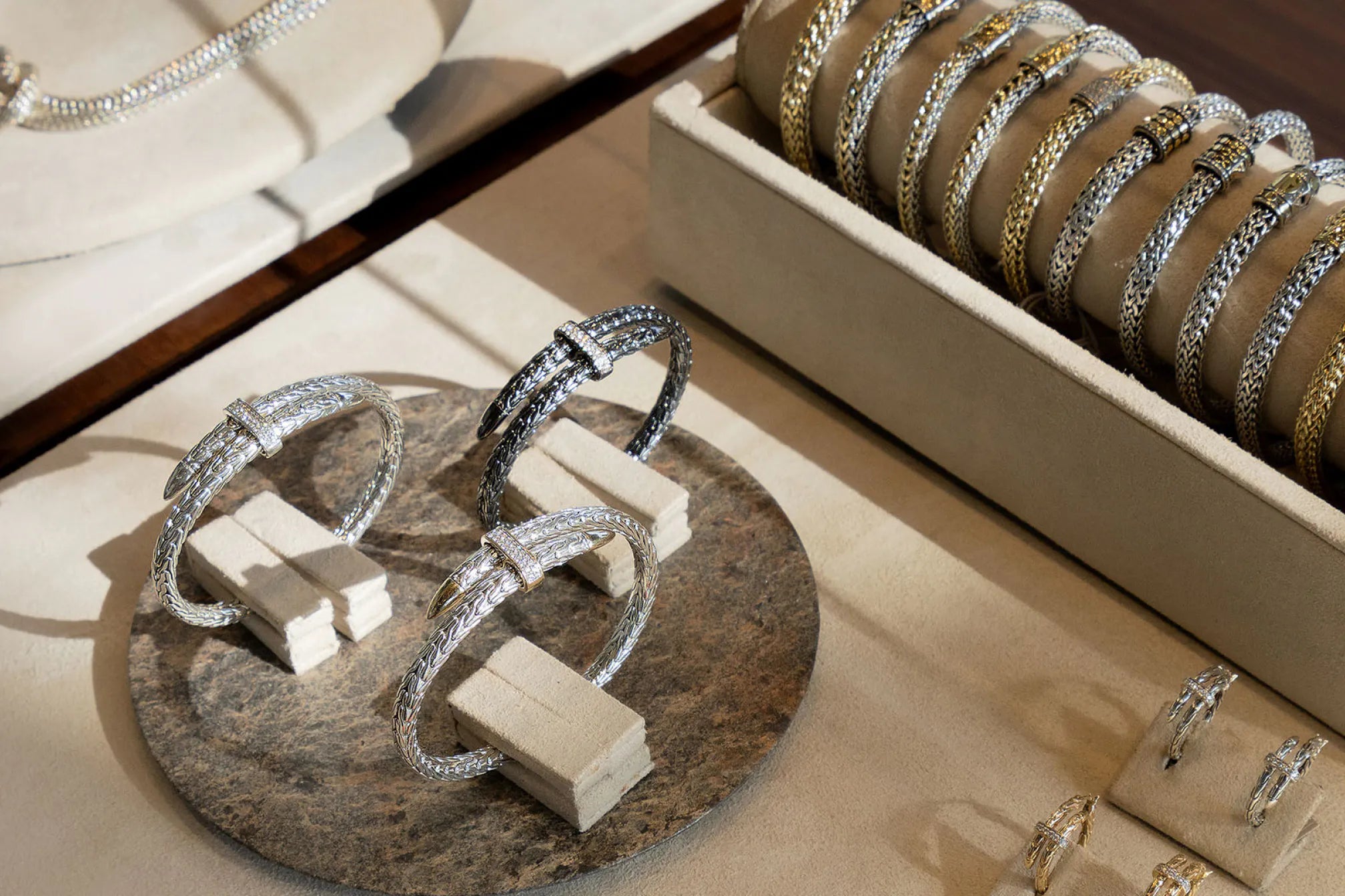 Silver rings displayed on a stone stand with bracelets in the background