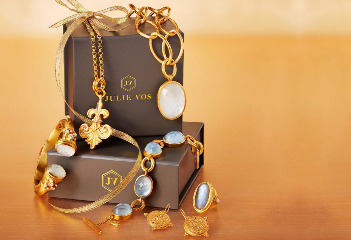 Gold jewelry set with gemstones on a branded box against a warm background