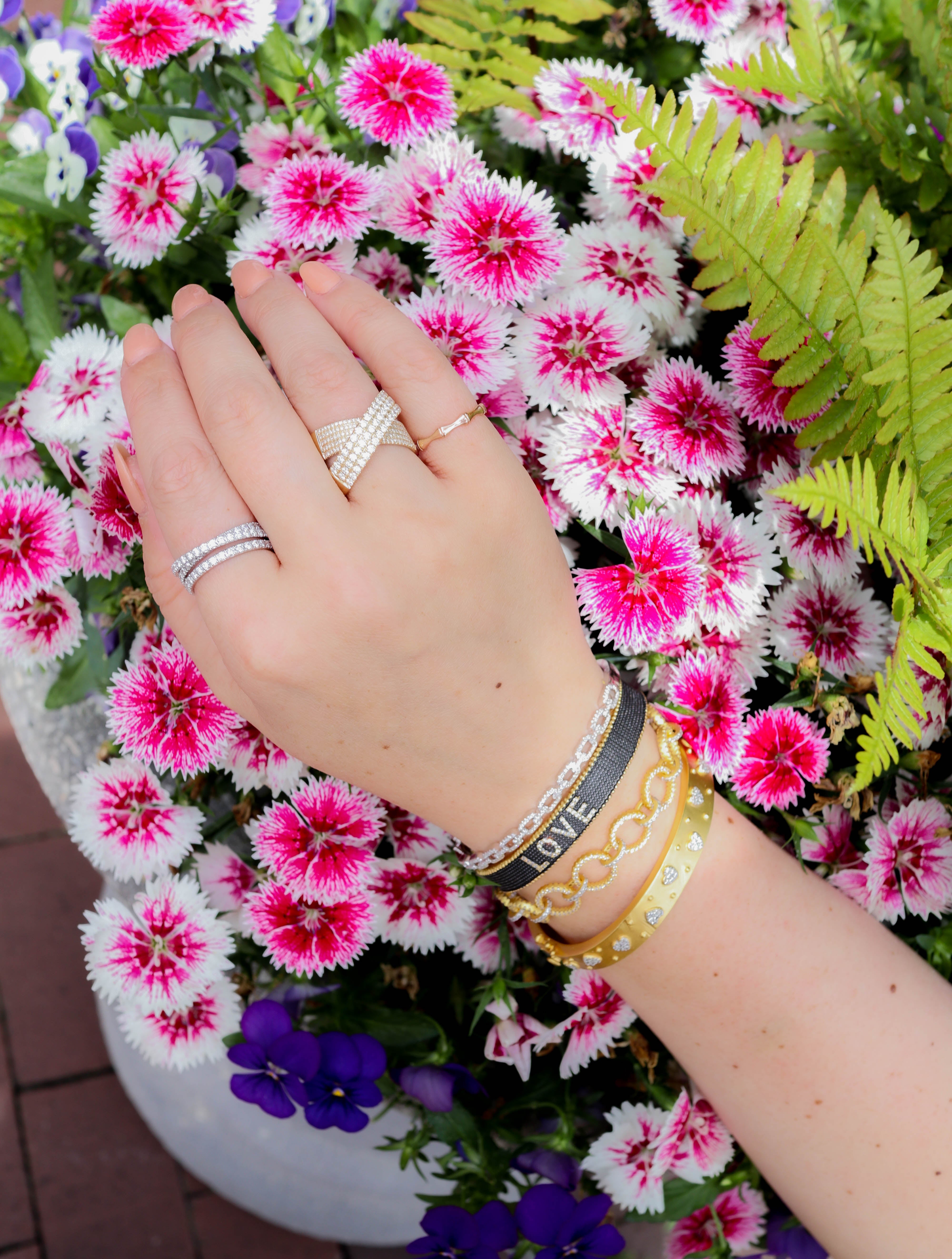 Hand with multiple rings and bracelets in front of pink and white flowers