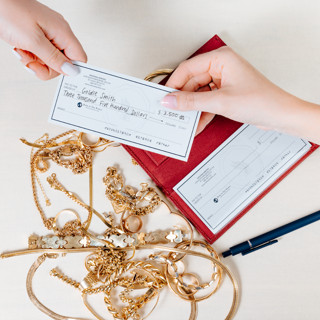 Two hands holding a check over a pile of gold jewelry on a light surface.