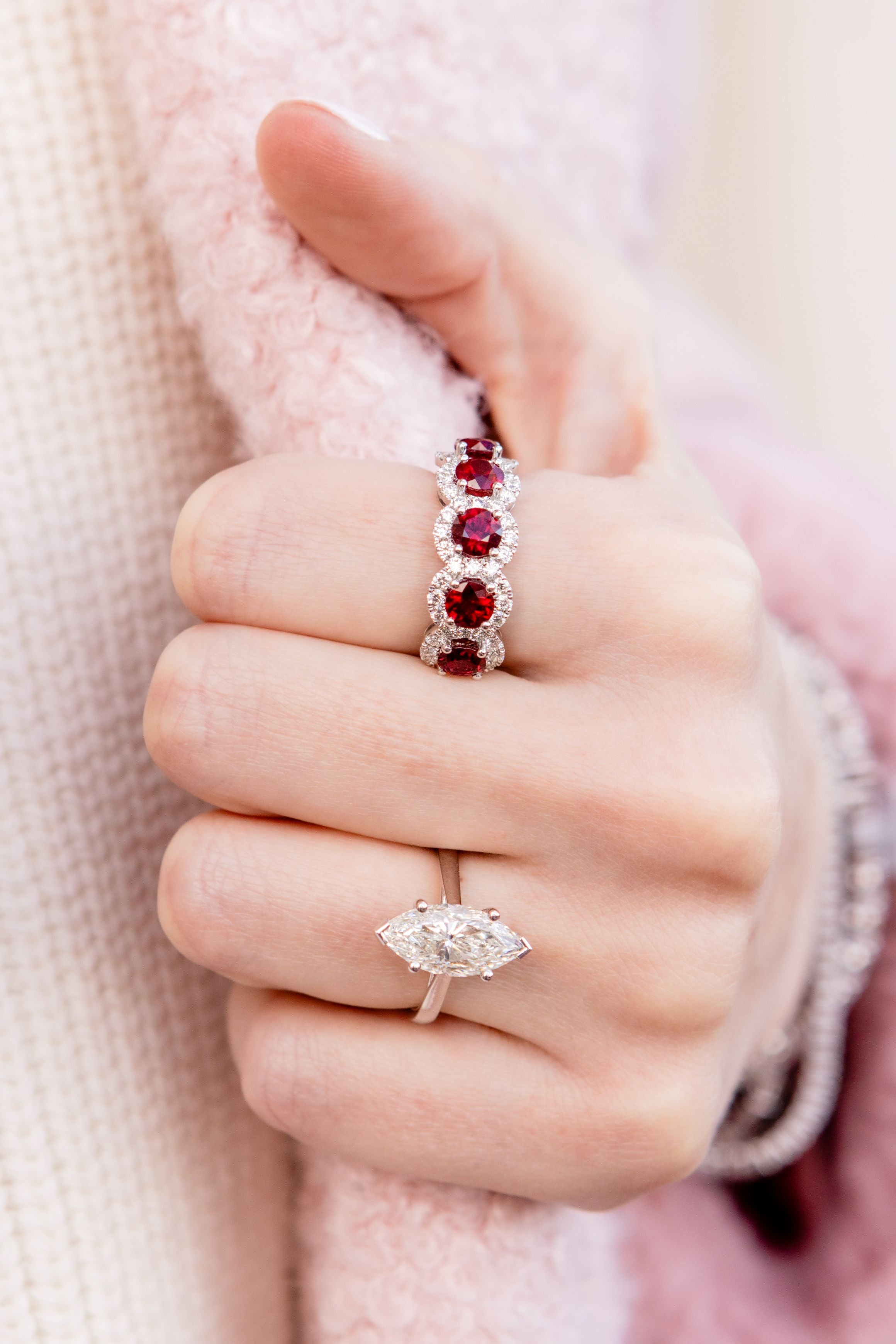 hand wearing diamond and red ruby rings with a light pink blurred background