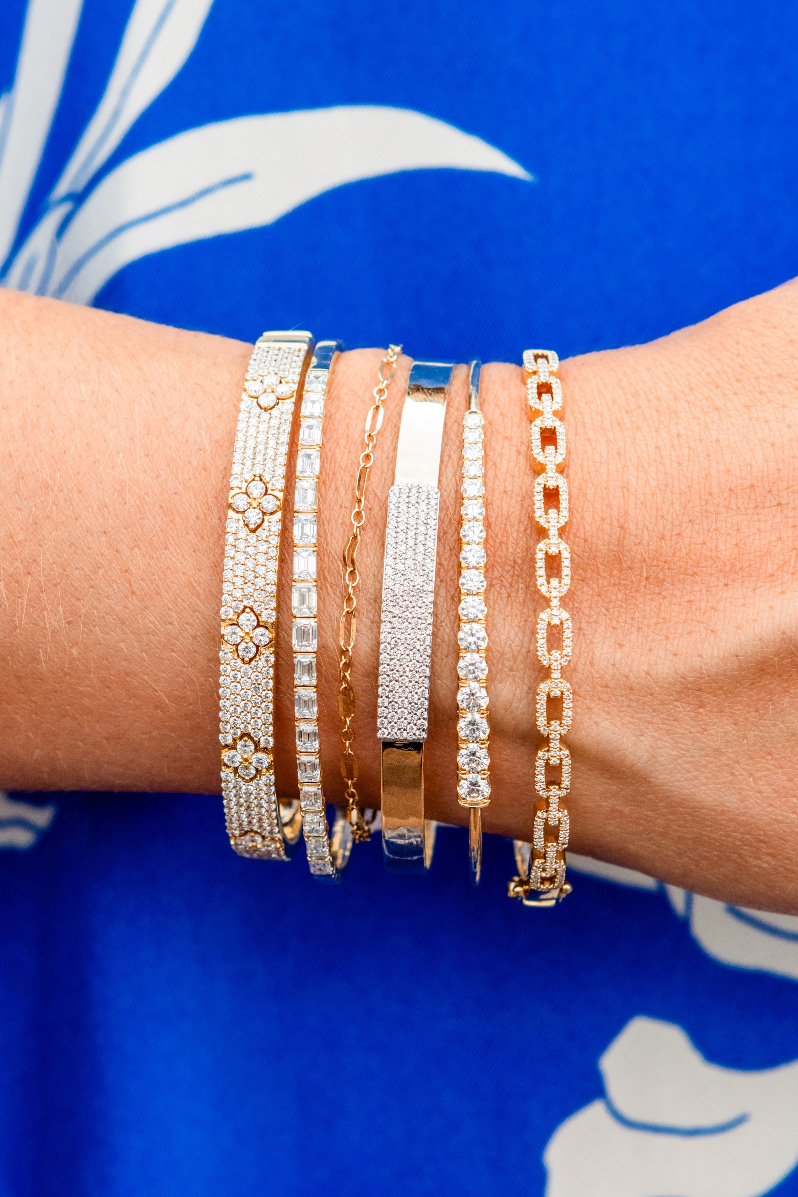 Close-up of a wrist wearing multiple gold and silver bracelets against a blue background