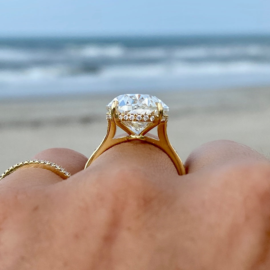 Gold ring with a large diamond held on a person's finger against a beach background