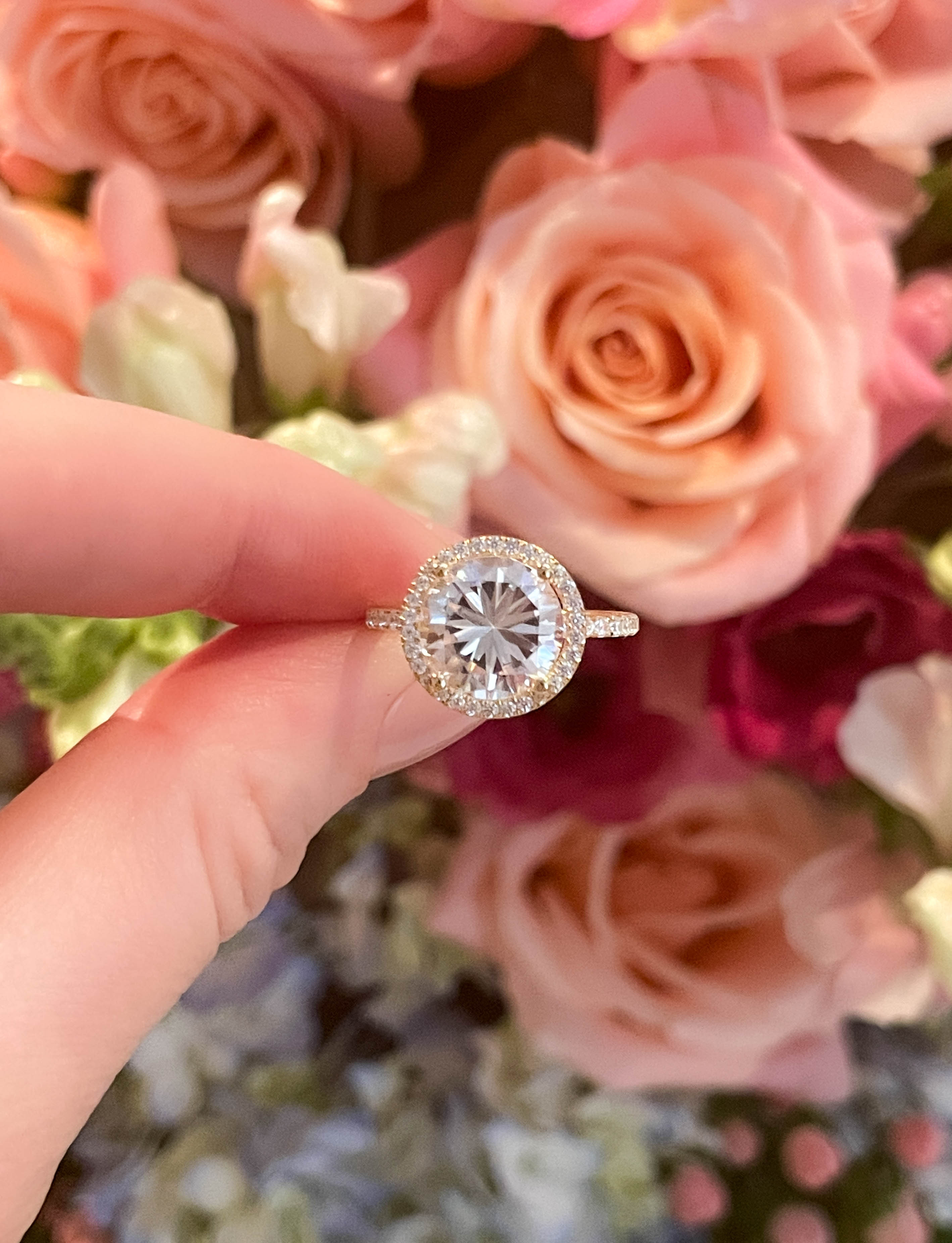 hand holding diamond ring with orange and red roses in the background