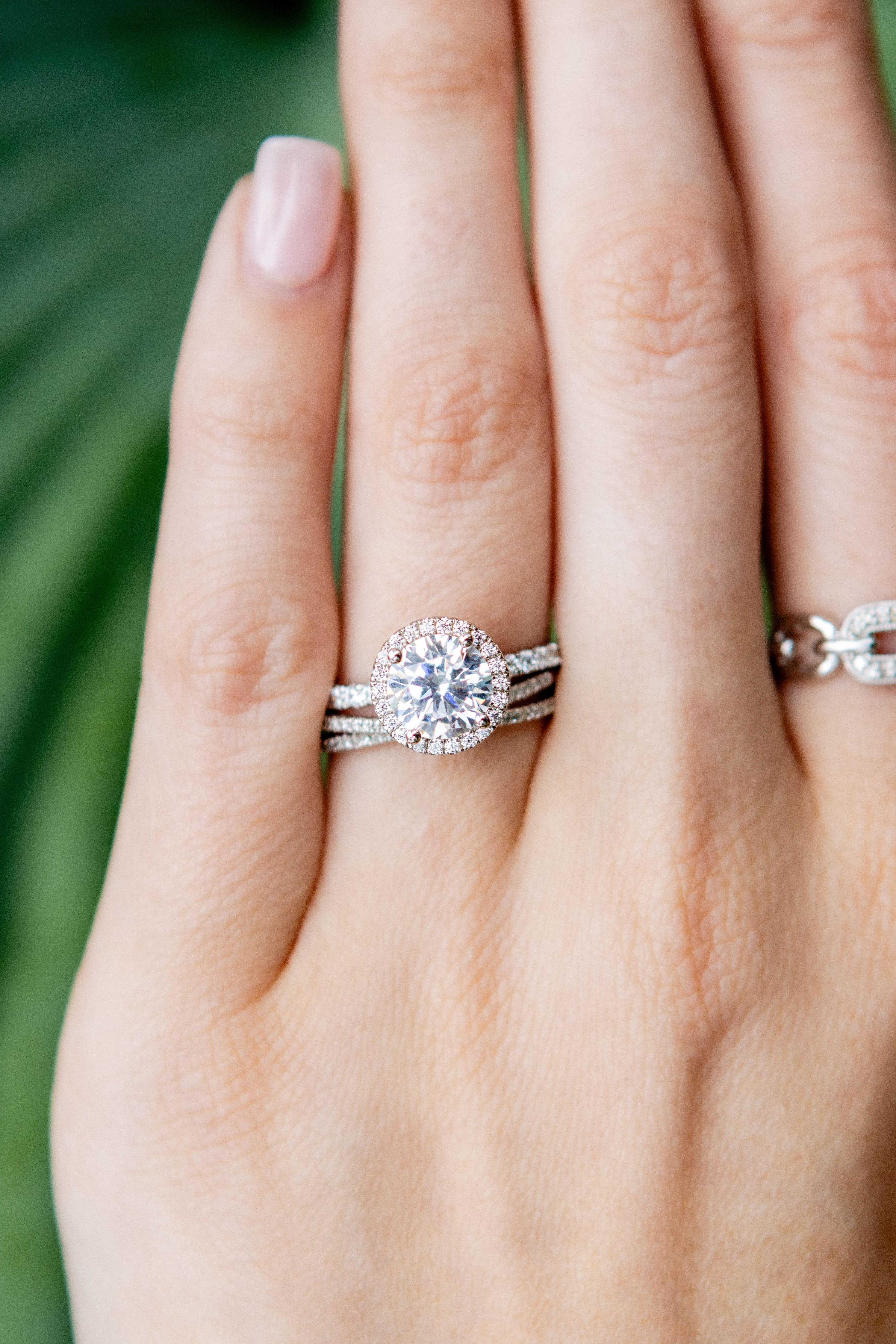 Close-up of a hand wearing two diamond rings with a blurred green background