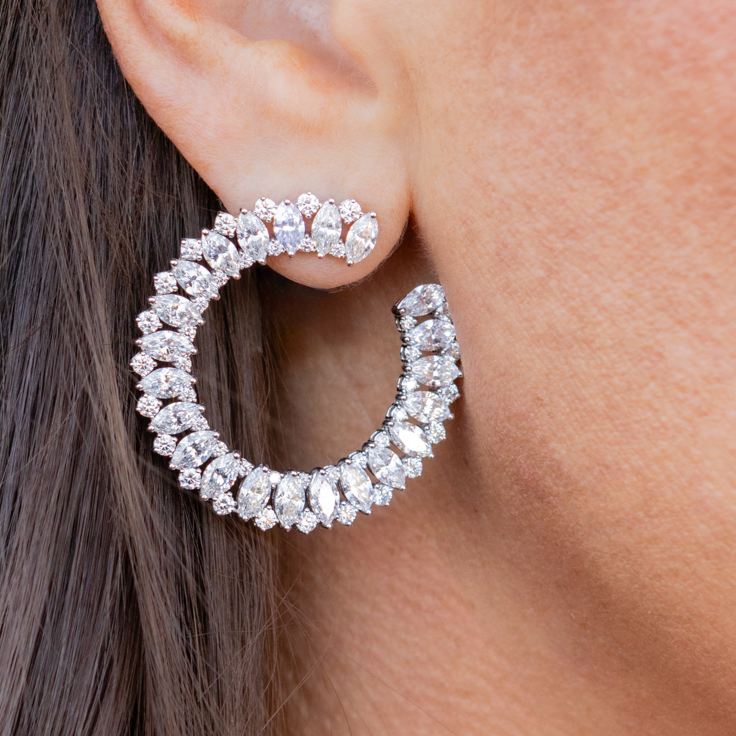 Close-up of a person wearing a silver hoop earring with clear gemstones.