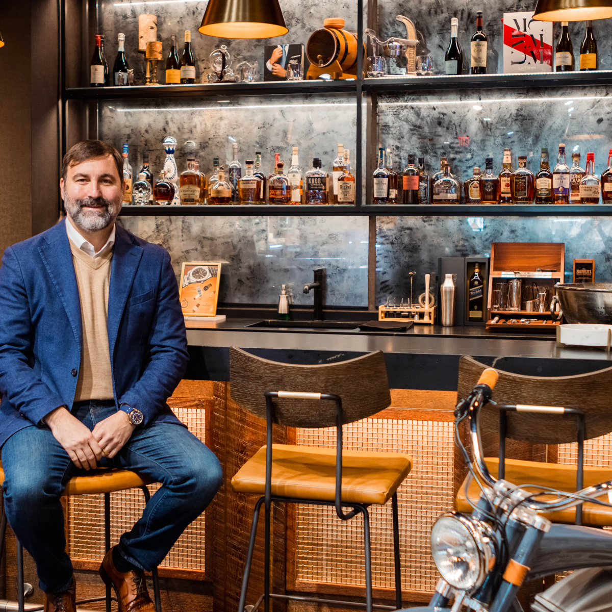 Man sitting at a bar with a well-stocked shelf behind him