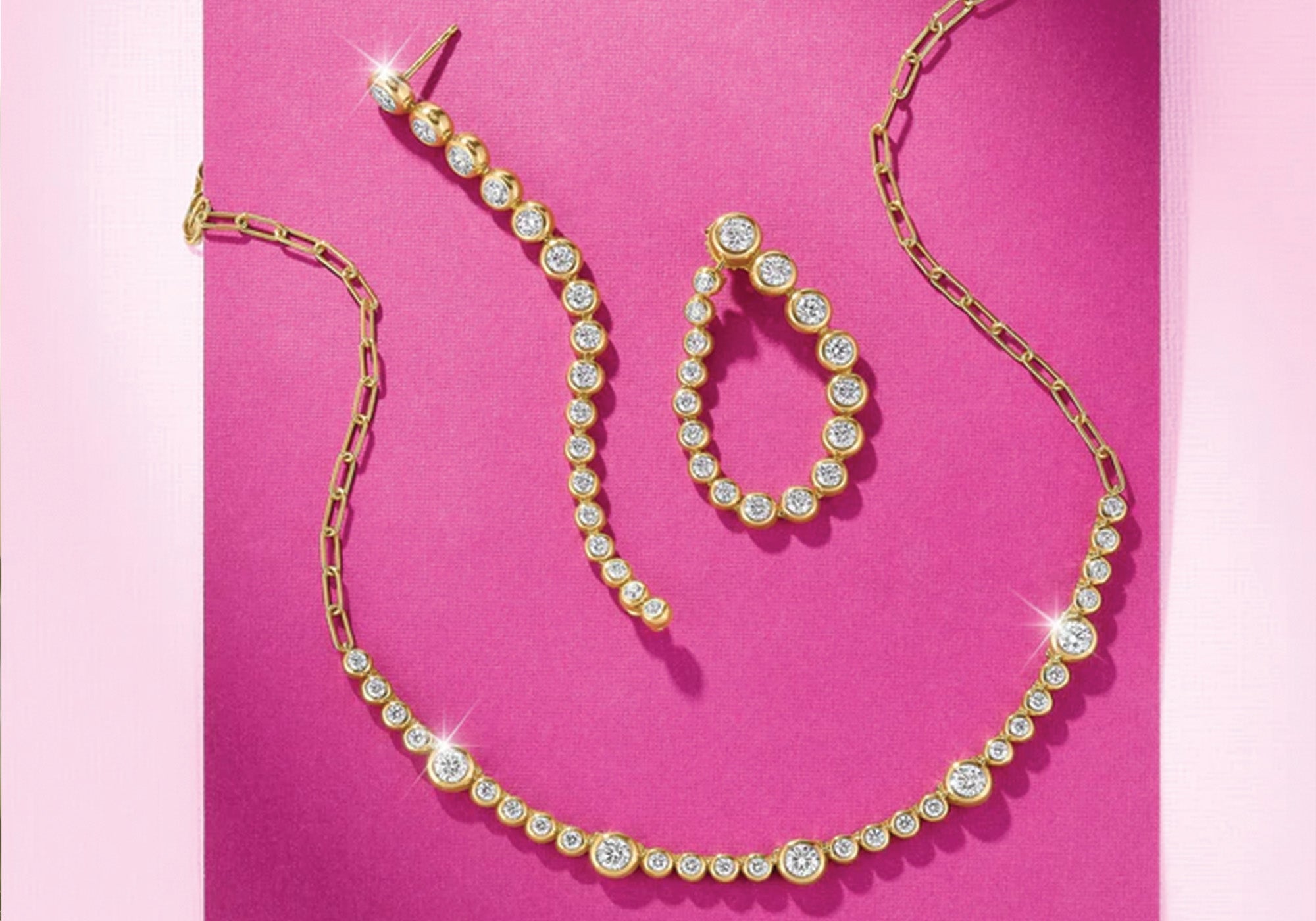 Gold necklace and earrings on a pink background