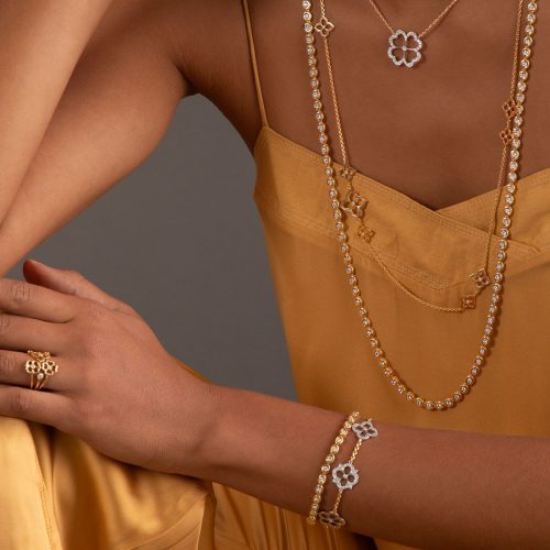 Person wearing a necklace, ring, and bracelet with floral designs on a neutral background