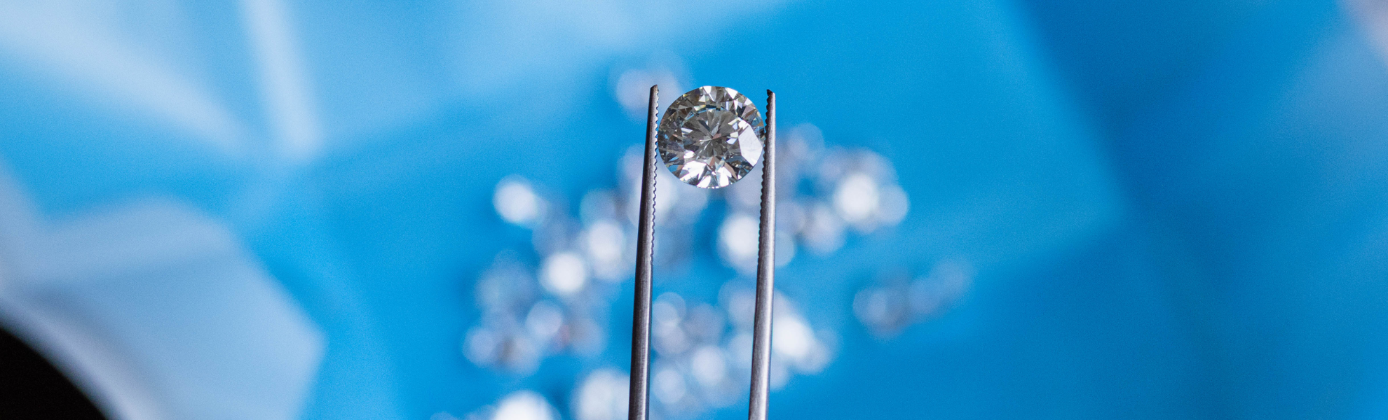 Diamond held between tweezers against a blue background