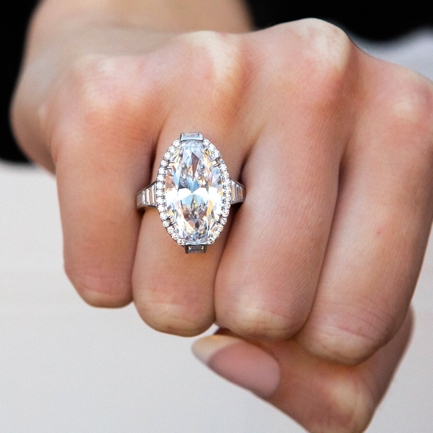 Close-up of a hand wearing a silver ring with a large diamond on a neutral background