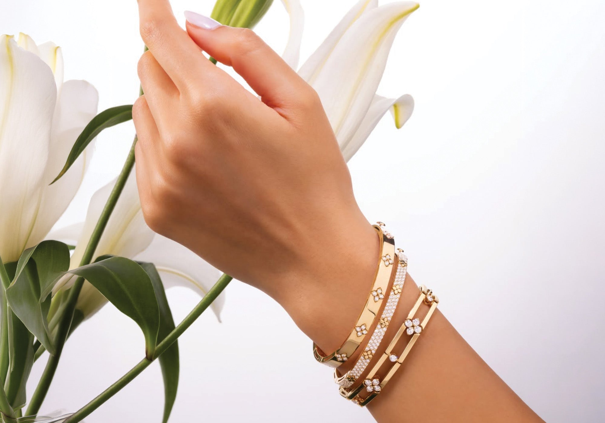 Hand wearing gold bracelets with a background of white lilies