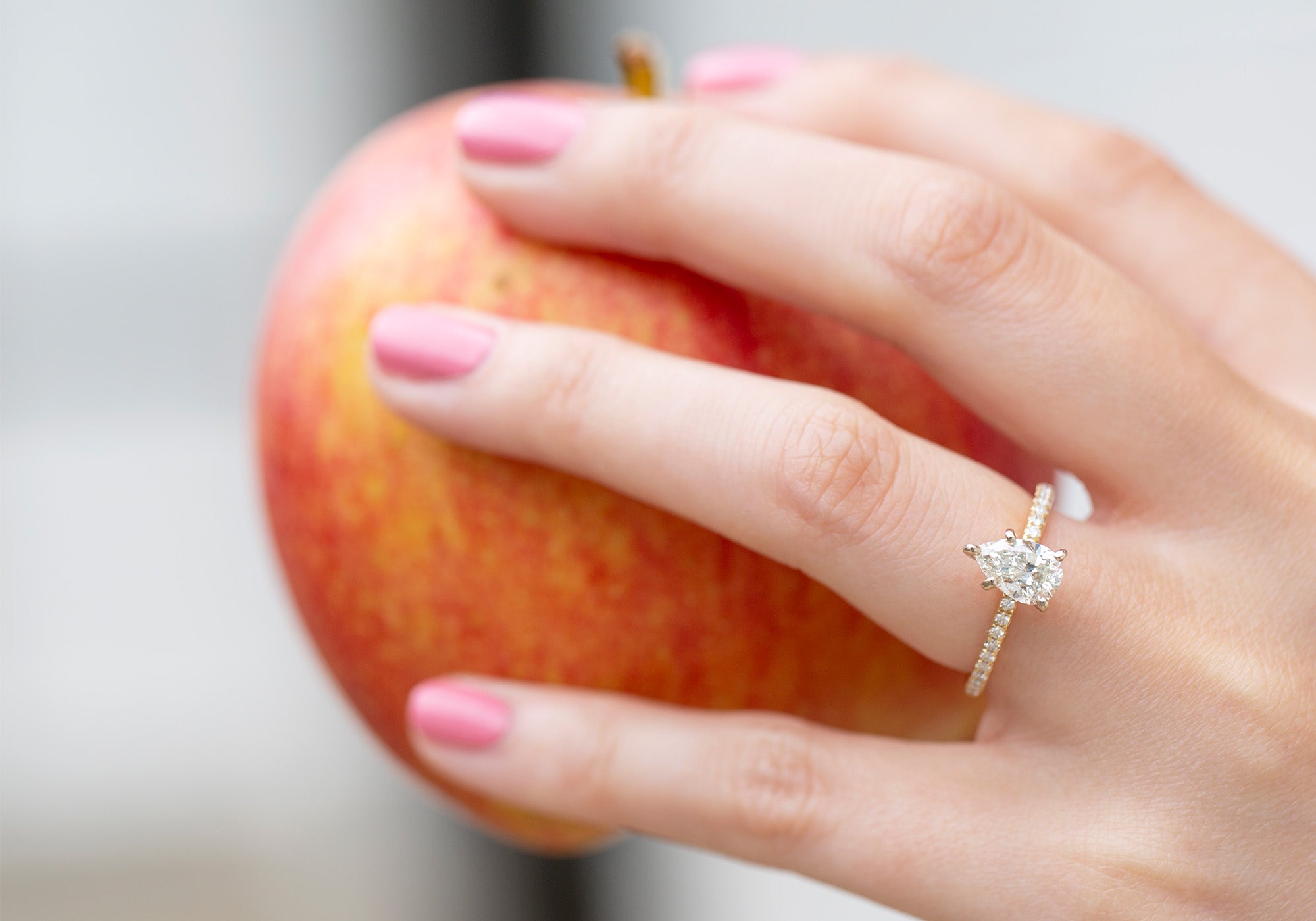 Hand holding an apple with a diamond ring on a blurred background