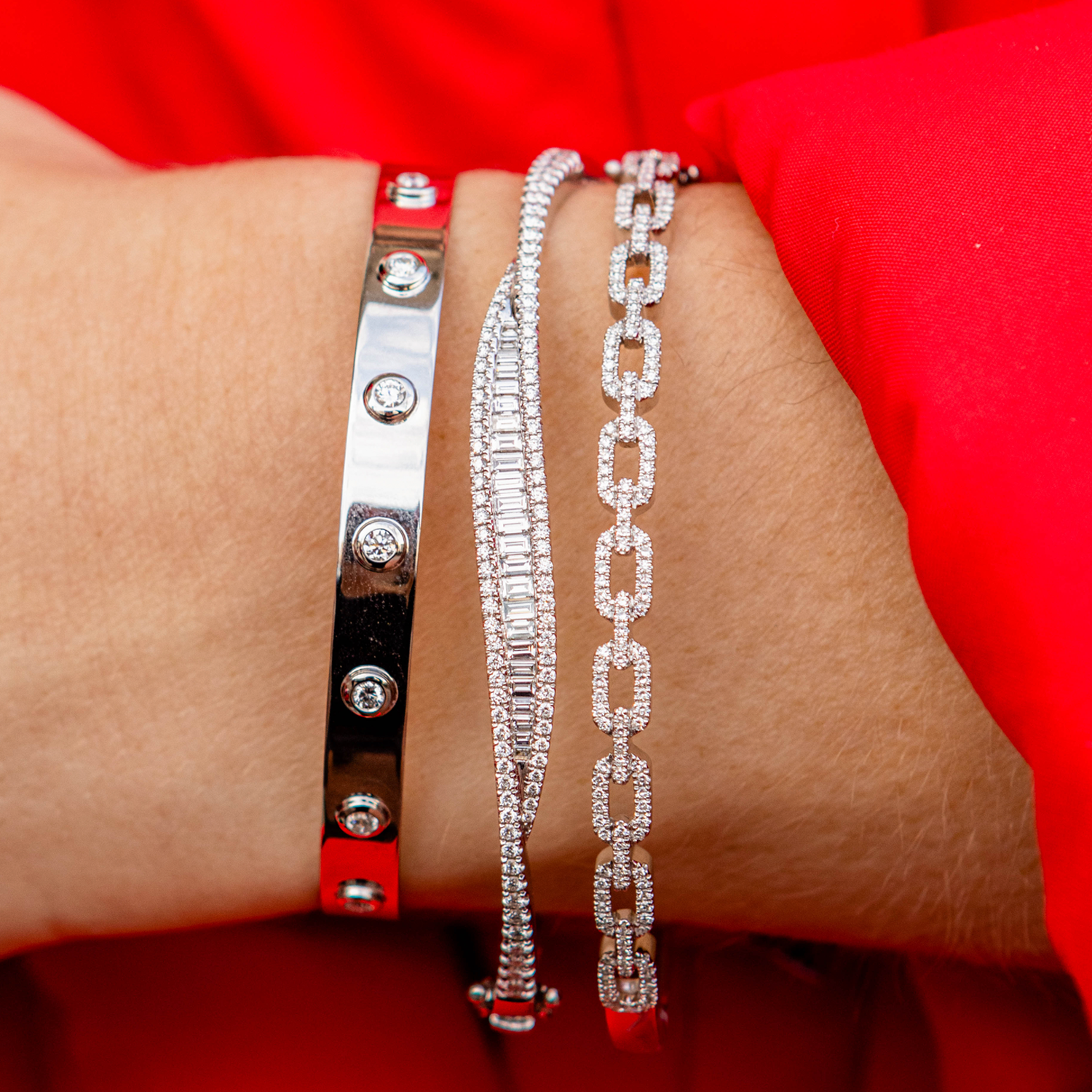 Three silver bracelets on a wrist against a red background