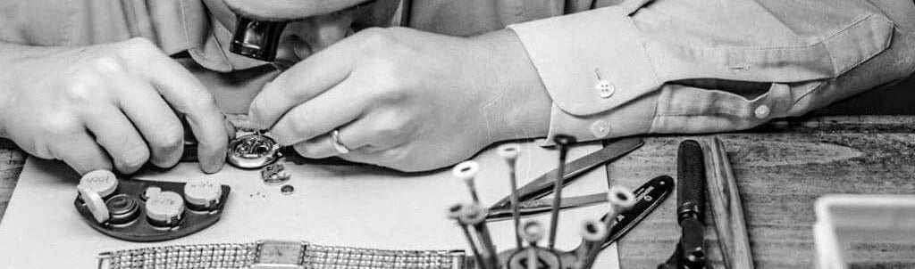 Person working on a small mechanical object with tools on a wooden surface