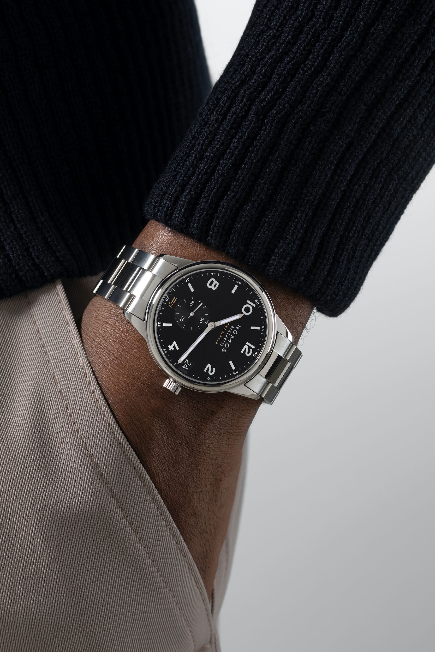 Close-up of a wrist wearing a silver watch with a black face on a neutral background