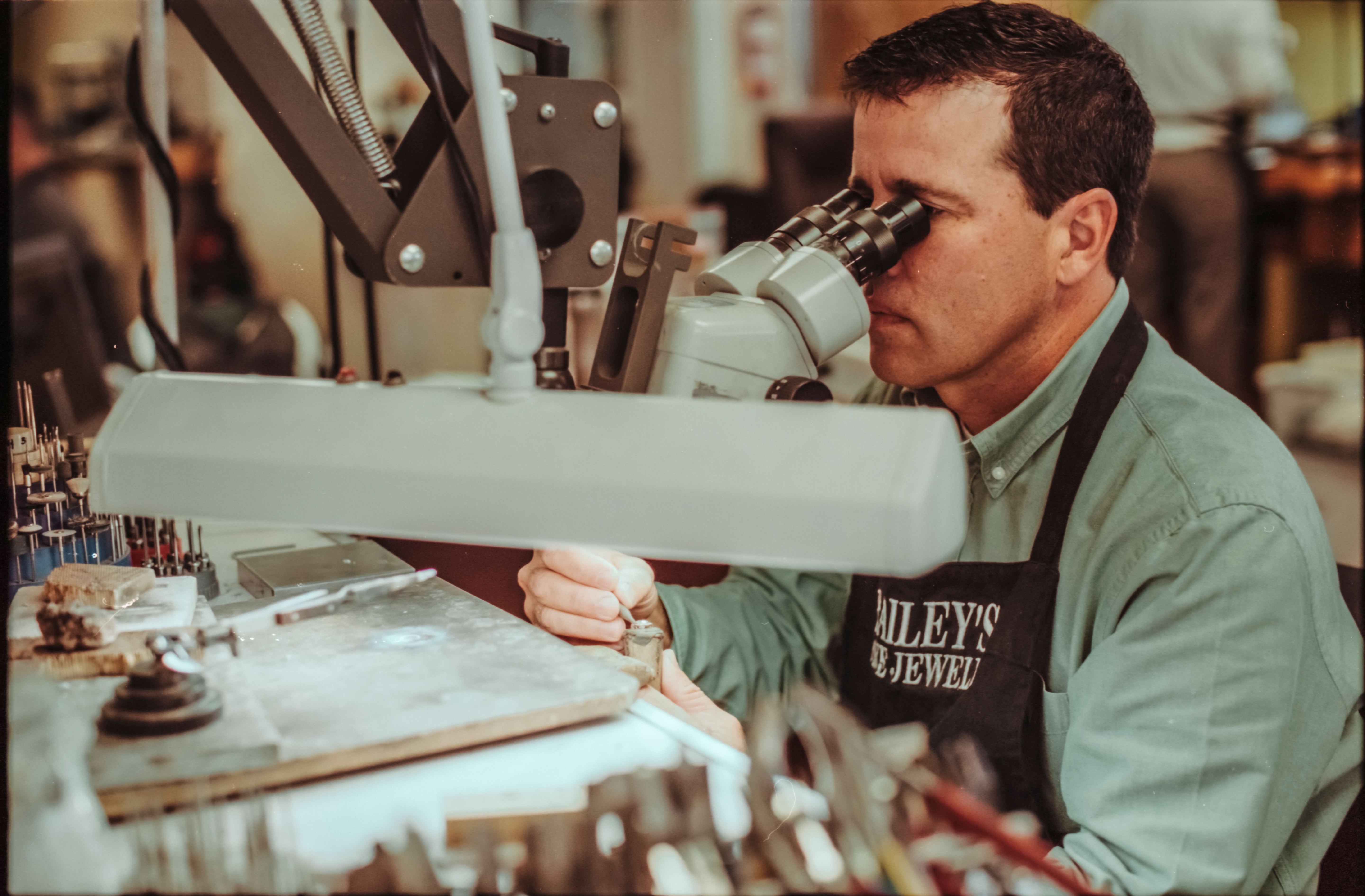 Man working with jewelry under a microscope in a workshop setting.