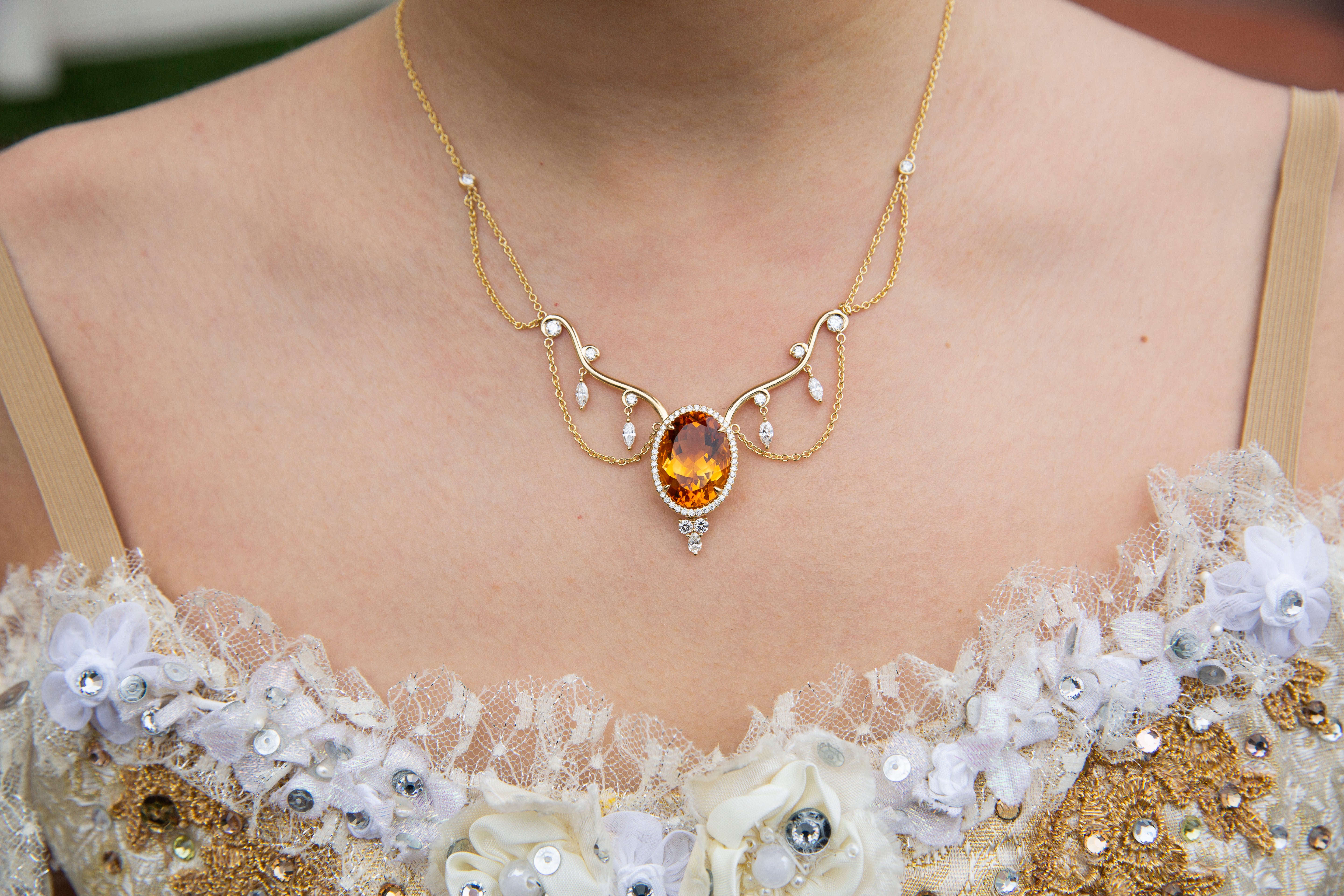 Close-up of a gold necklace with a amber stone on a person wearing a floral dress.