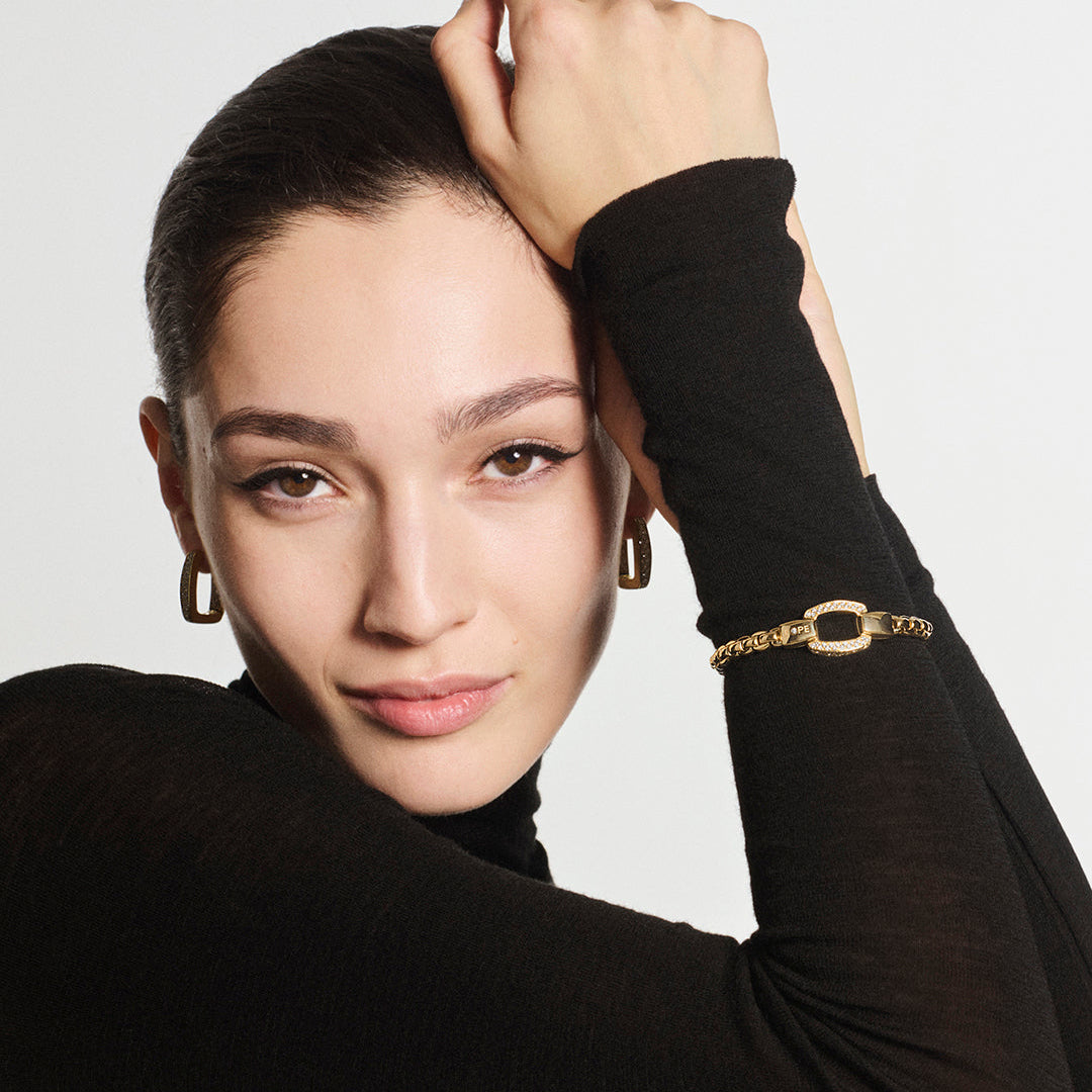 Woman wearing a black turtleneck and gold bracelet against a light gray background