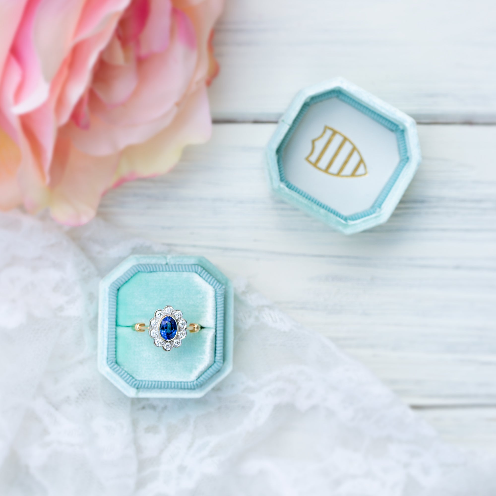 blue sapphire and diamond ring in a blue hexagonal box on a white surface with a pink rose