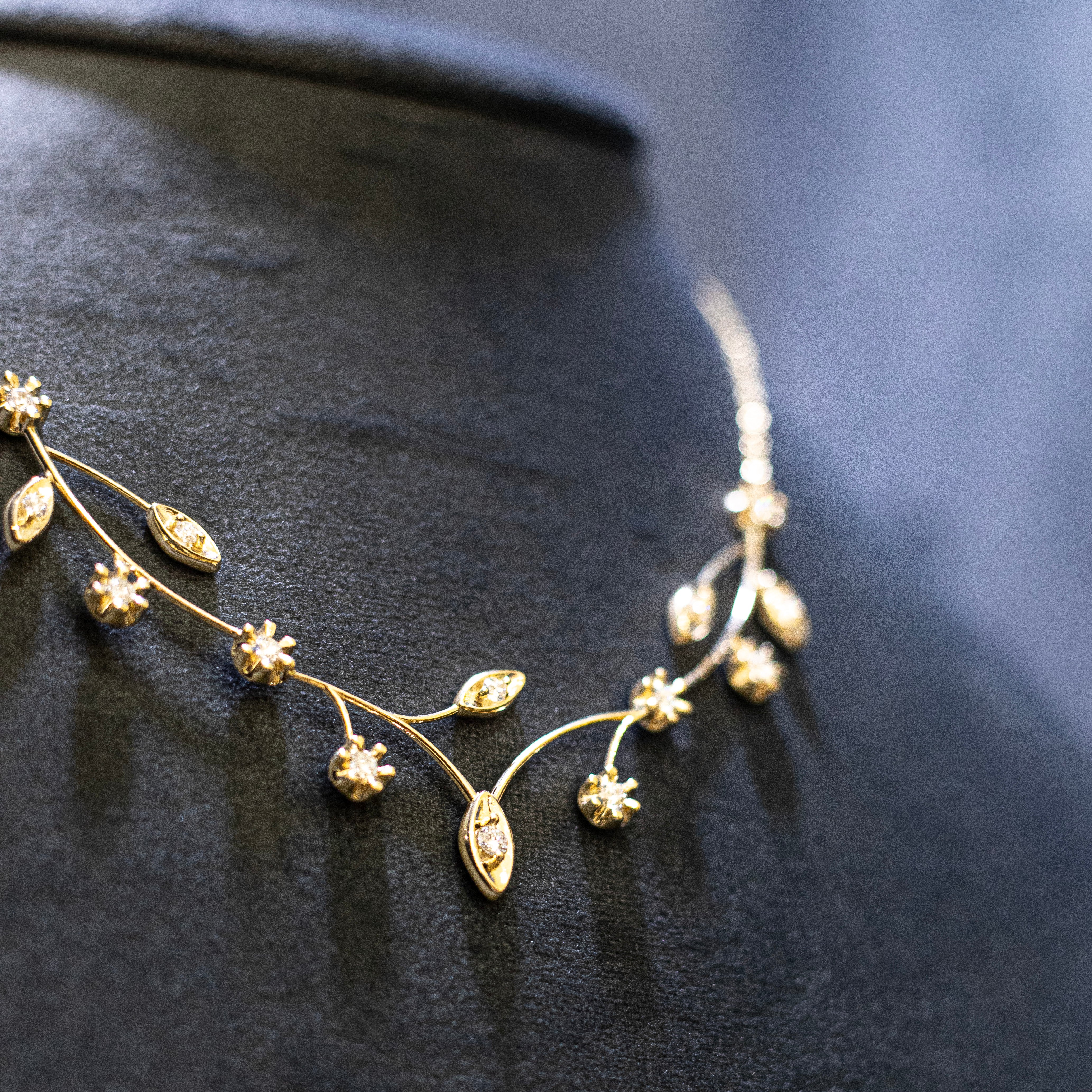 custom gold necklace with flowers and leaves against black background